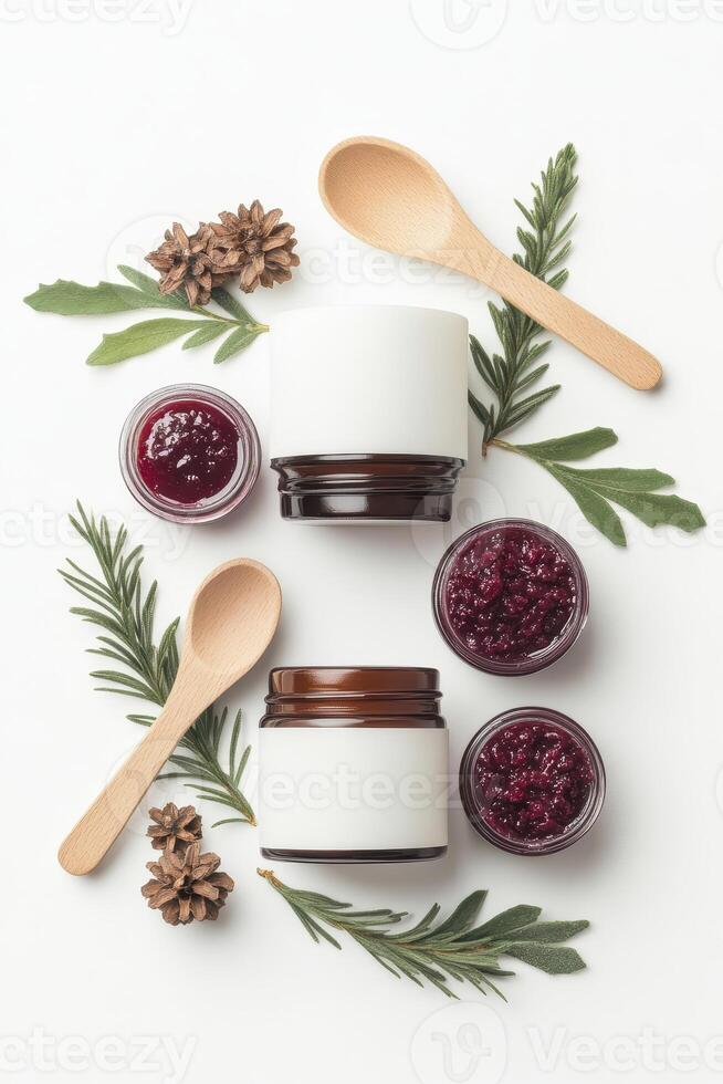 Jars with red jam sit near wooden spoons and evergreen branches with pine cones on a white surface viewed from above photo