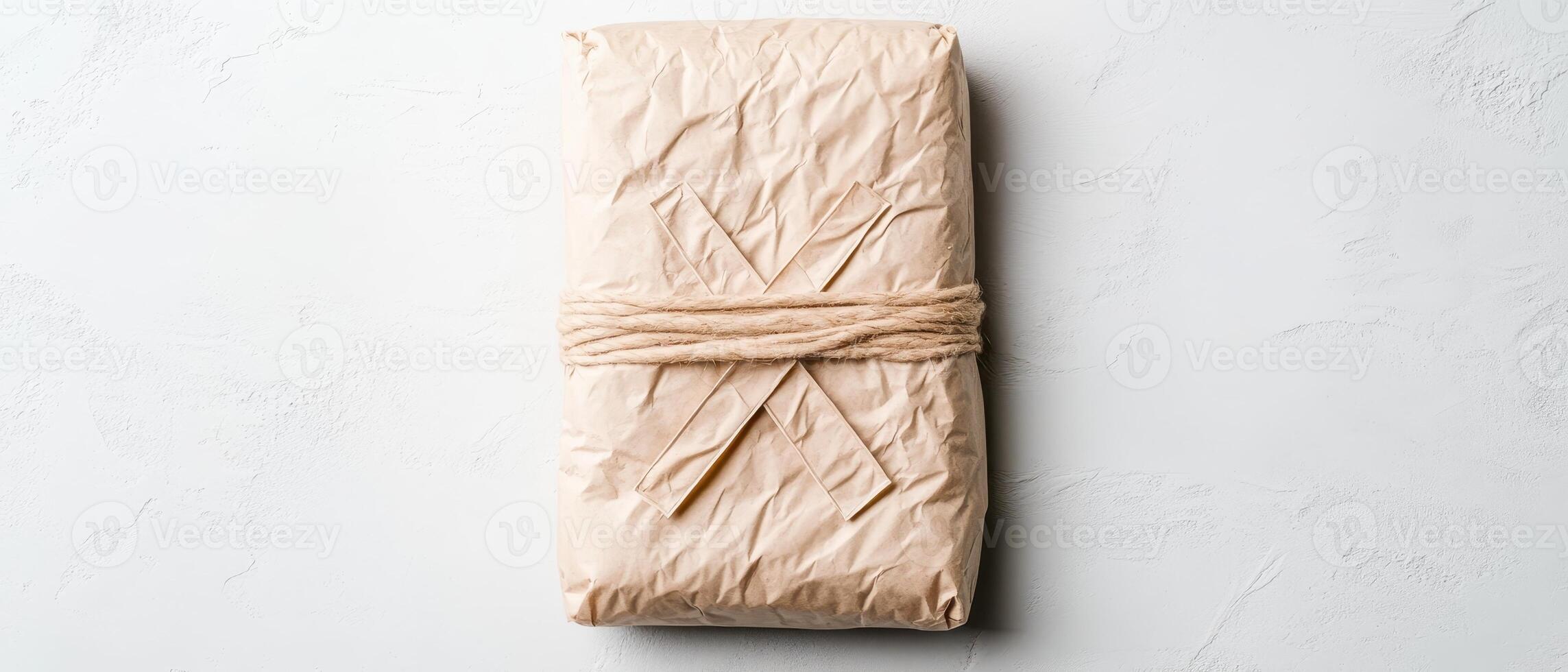 Wrapped package on a neutral surface. Brown paper held with simple twine. Rectangular form. Plain covering. Rustic wrapping. Minimalist aesthetic. Top view arrangement. photo