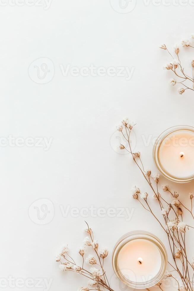 Burning candles in glass jars near small dried white flowers on a simple white surface providing quiet warmth and soft decorative accents photo