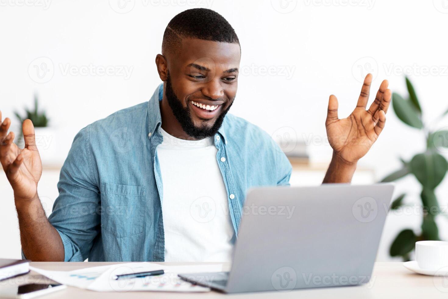 Happy Black Freelancer Man Celebrating Success While Working Online On Computer, African Guy Looking At Laptop Screen, Raising Hands And Exclaiming With Excitement, Sitting At Desk In Home Office photo