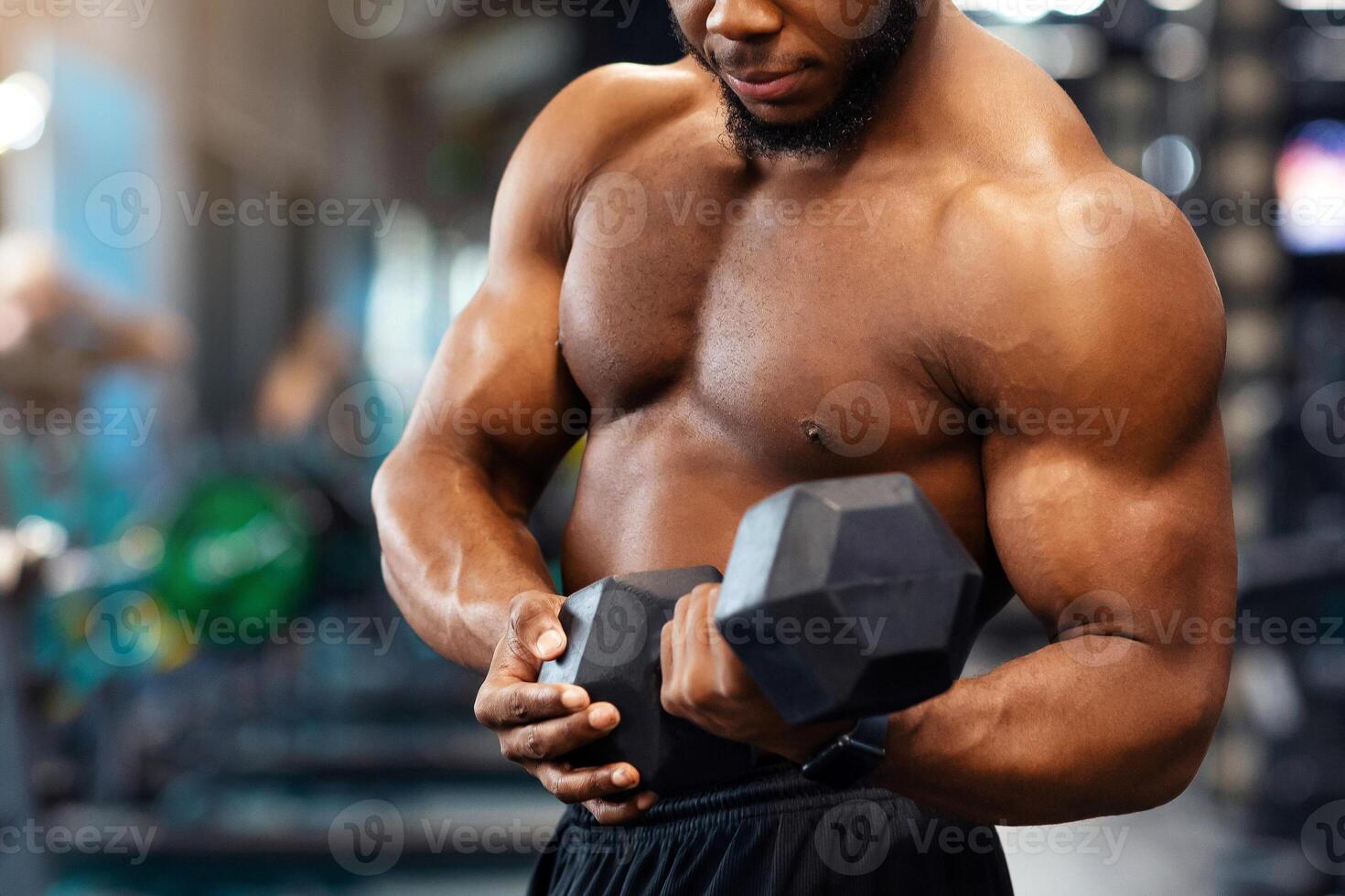 Biceps workout session. Concentrated african american shirtless athlete training arms with dumbbells at gym, empty space. Hot black bodybuilder working on his biceps, lifting barbell with one hand photo