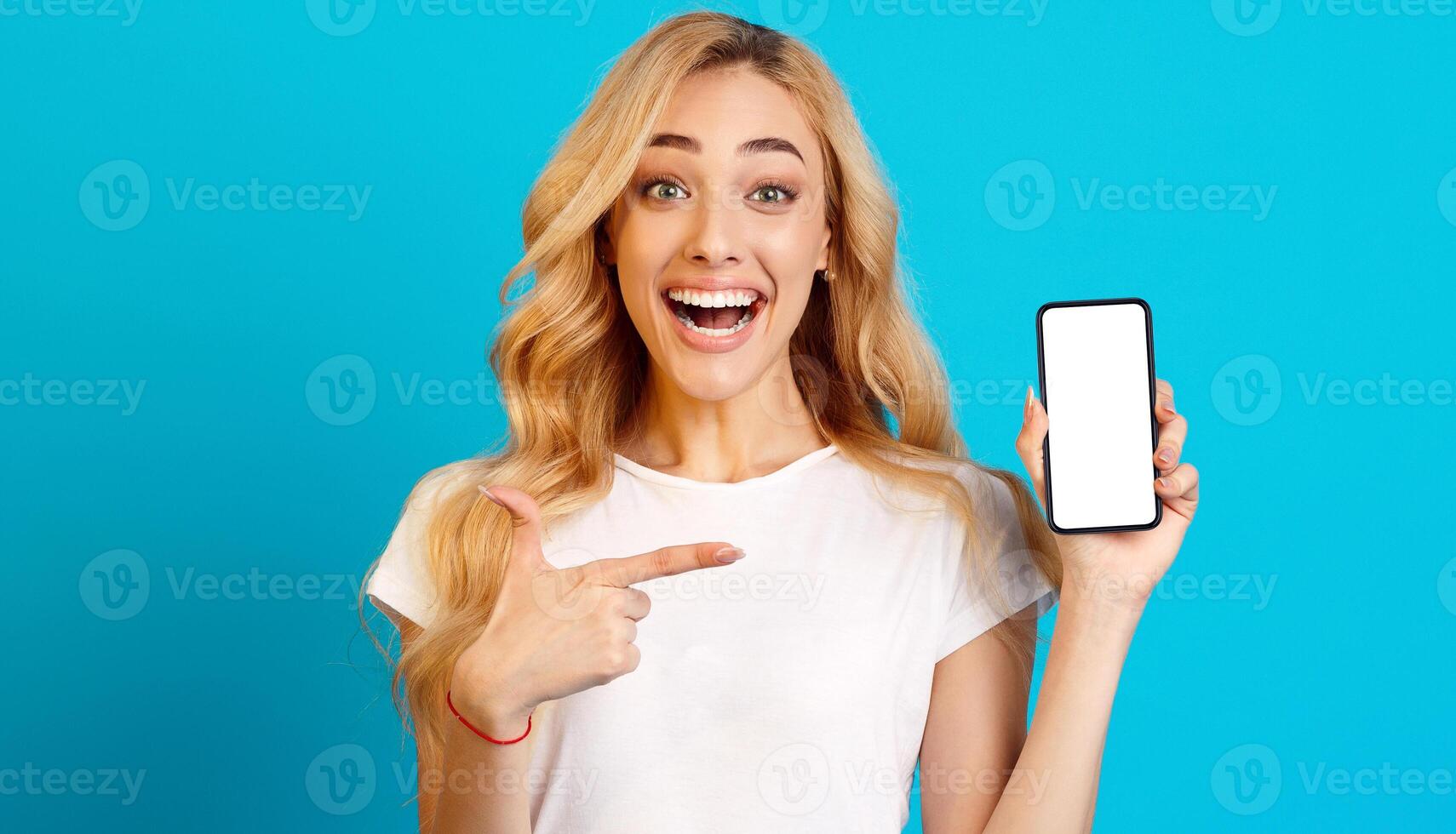 Millennial Woman Showing Phone with Blank Screen and Pointing On It, Blue Background photo