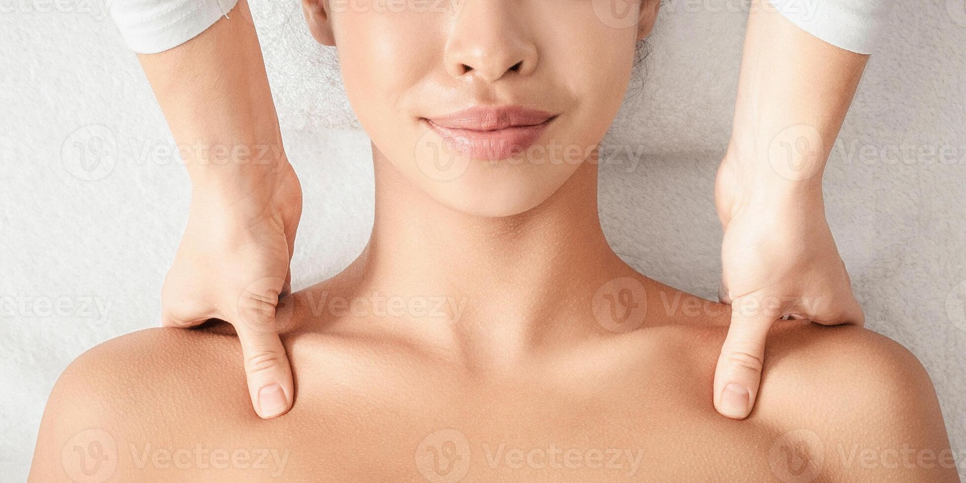 Spa Treatment. Relaxed Asian Woman Getting Wellness Shoulder Massage By Professional Masseur, Calm Korean Lady With Flower In Hair Lying On Table With Closed Eyes, Resting In Beauty Salon, Top View photo