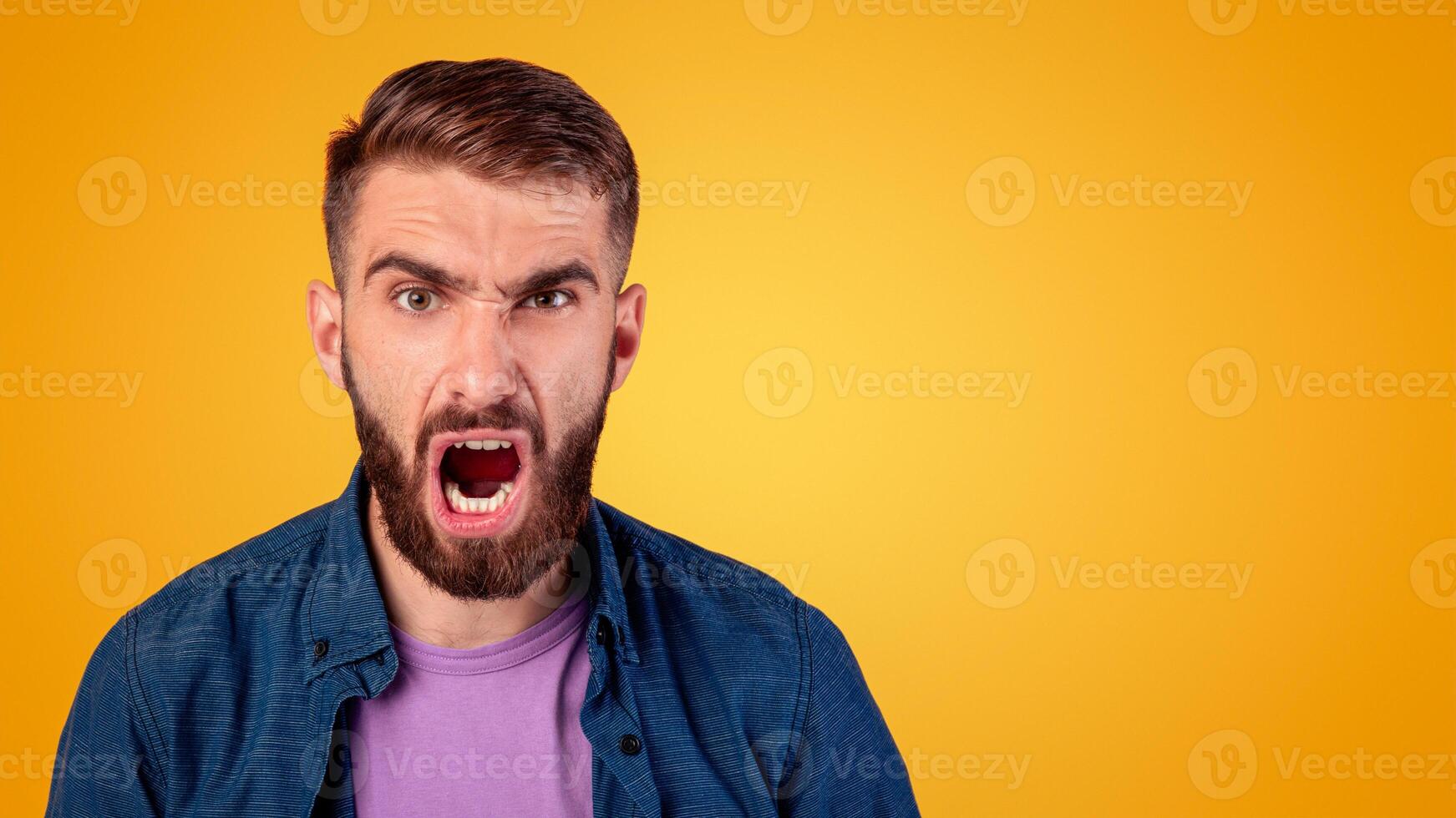 Portrait of young bearded guy shouting furiously, expressing his anger over grey studio background. Annoyed millennial man screaming, feeling enraged and aggressive. Negative emotions concept photo