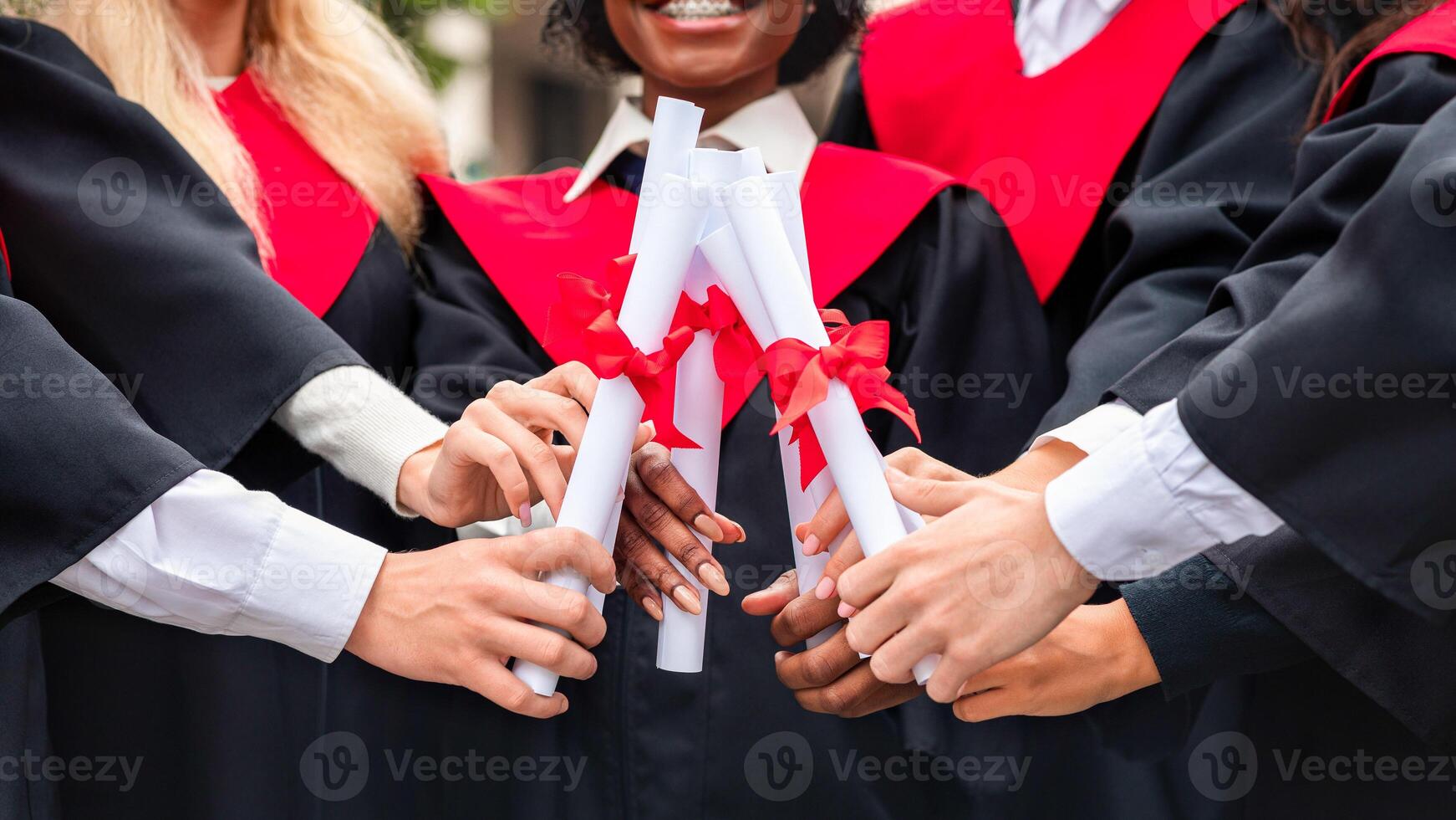Cropped of multiracial group of students in graduation caps and robes posing at university campus, joining together their diplomas, celebrating graduation, closeup. Graduation concept photo