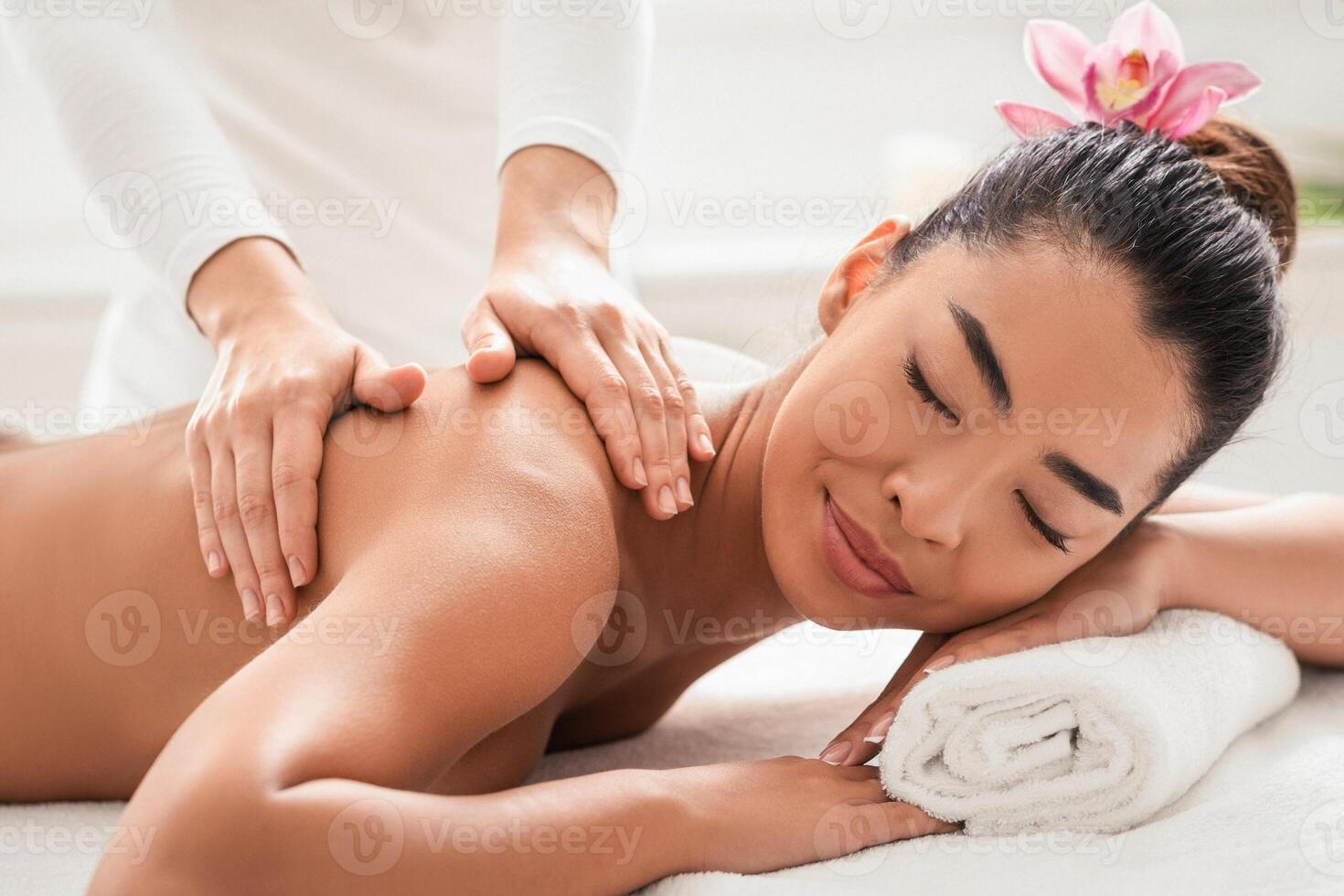 Relaxed Asian Woman Pampering Herself With Body Massage In Spa Salon, Getting Professional Treatment With Masseur, Lying On Table With Closed Eyes, Enjoying Wellness Day At Beauty Parlor photo
