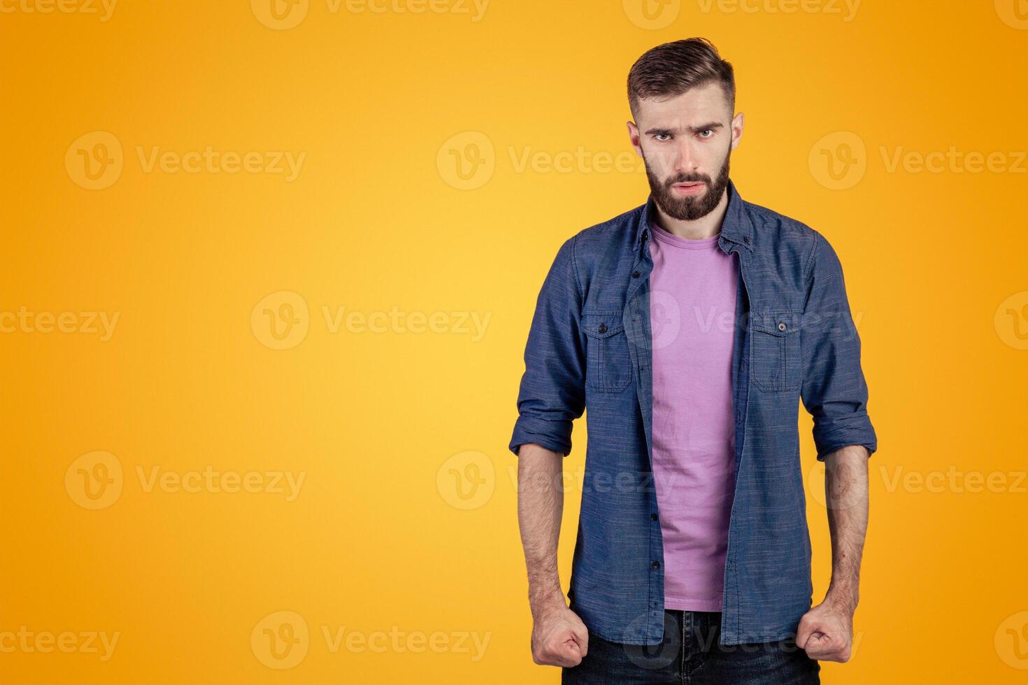 Furious young man clenching his fists, suppressing his anger on grey studio background. Aggressive millennial guy ready for fight or conflict. Human negative emotions concept photo