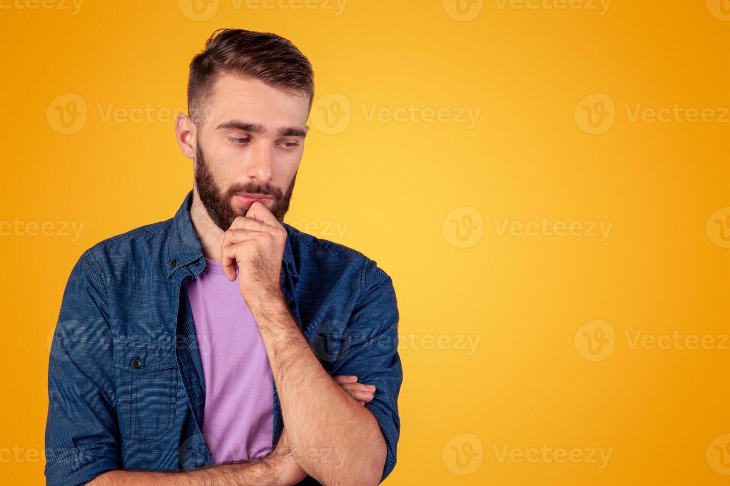 Dreamy young guy thinking over problem, touching his chin on grey studio background. Millennial hipster man making hard choice or decision, imagining something, having doubts photo