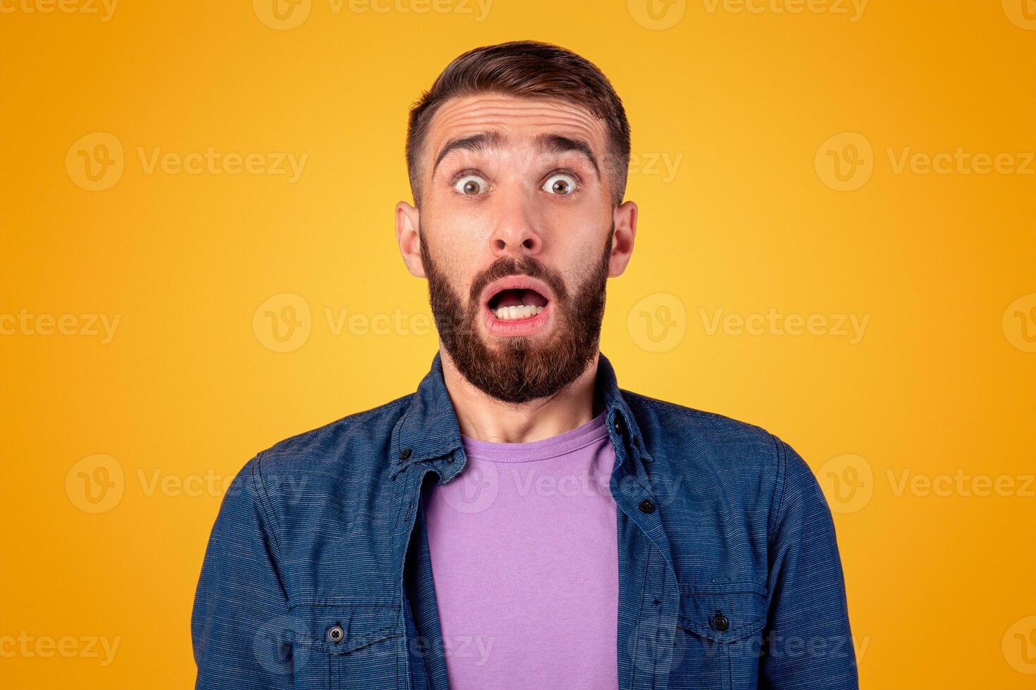 Shocked bearded guy looking at camera in panic over grey studio background. Frightened young man feeling opening mouth in surprise, feeling afraid or nervous, acting worried photo