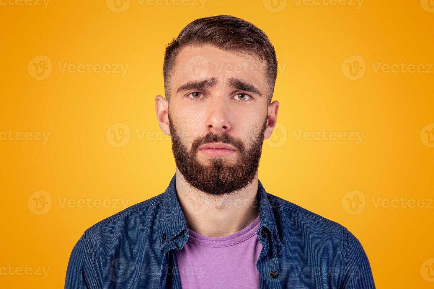 Millennial hipster guy feeling sad, lonely or depressed on grey studio background. Melancholic bearded man with unhappy face expression having trouble, suffering from stress or personal crisis photo