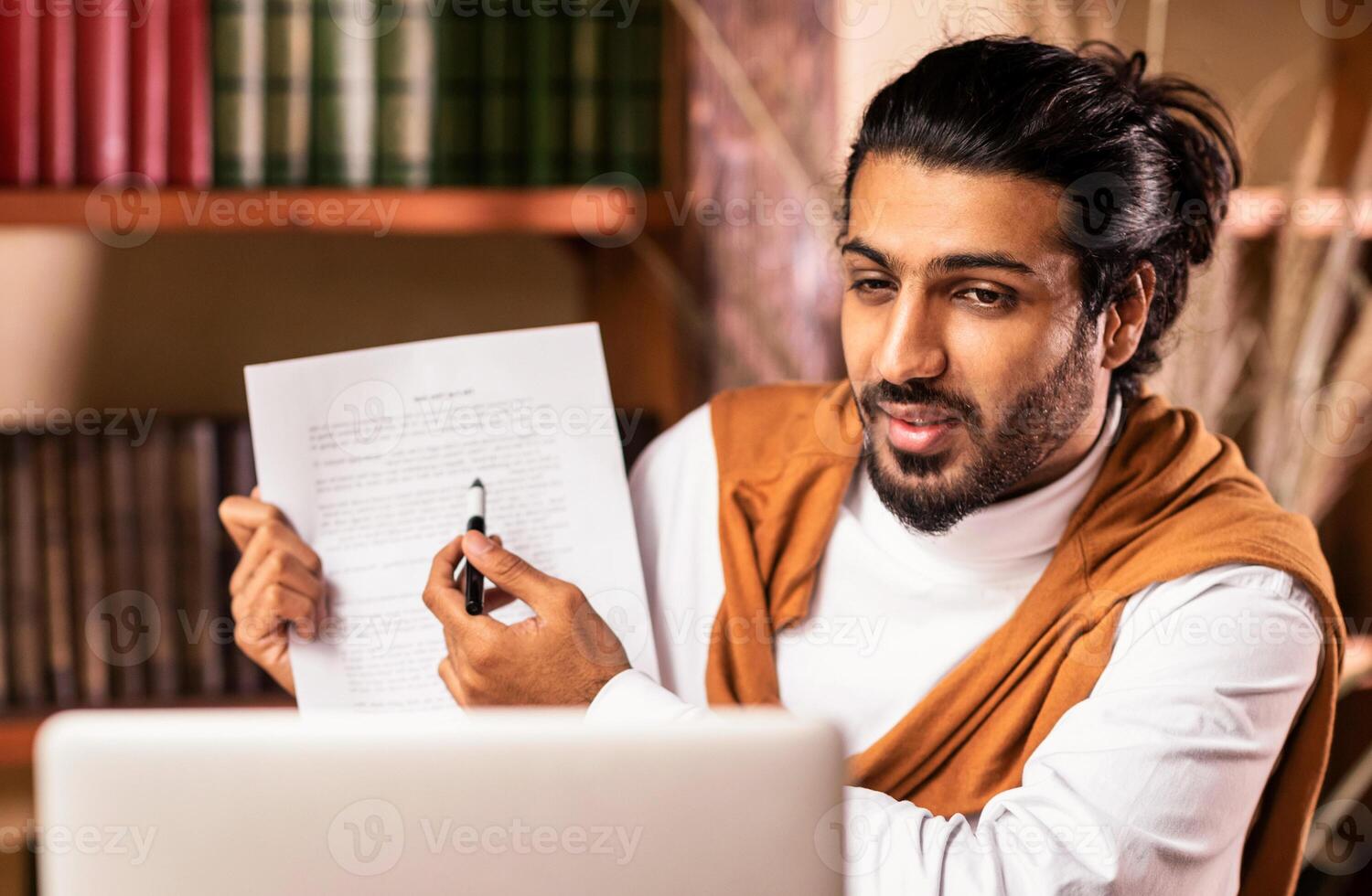 Distant Teaching. Indian Teacher Guy Having Class Via Call E-Teaching Remotely Showing Notebook To Laptop Webcam Explaining Lecture Sitting Indoors. Modern Tutoring And Education photo