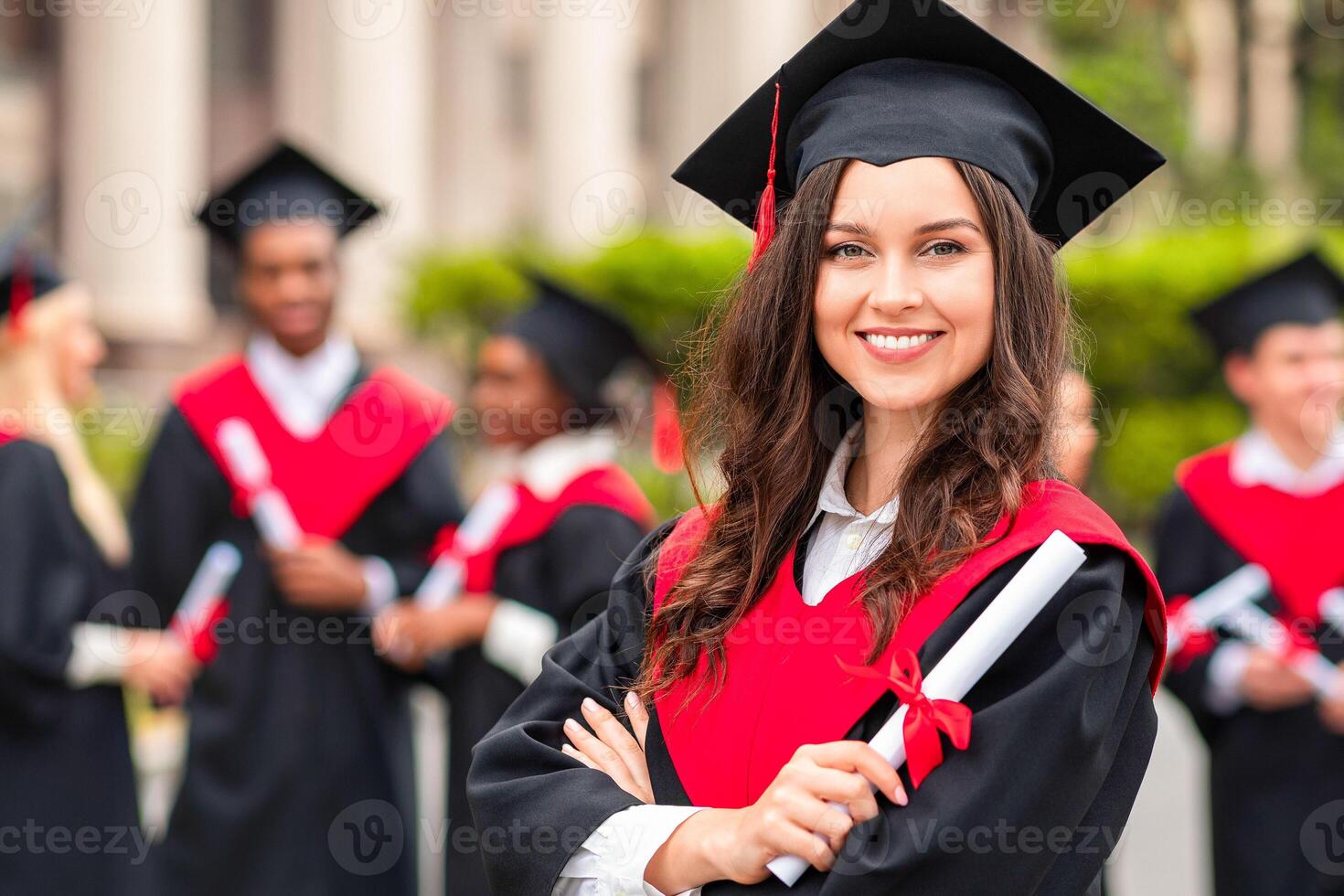 Positive pretty young lady student having graduation party, wearing graduation costume and holding diploma, happy female graduate proudly posing at university campus, blurred background photo