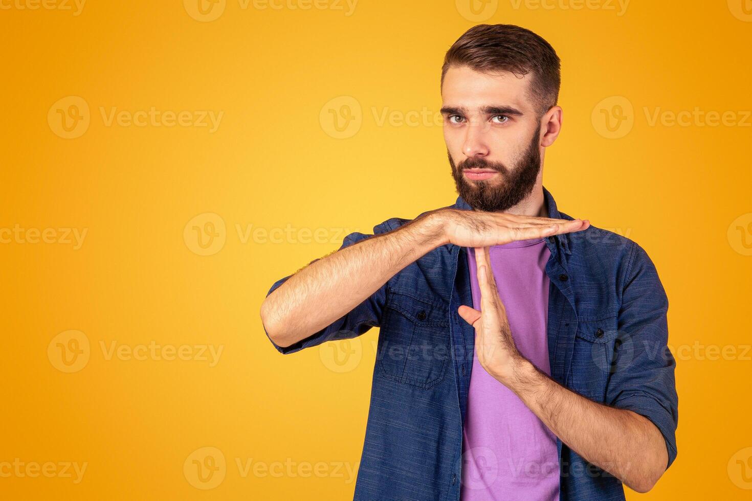Millennial bearded guy showing TIME OUT or STOP gesture over orange studio background. Young Caucasian man taking break or pause, running late, facing deadline, expressing rejection photo