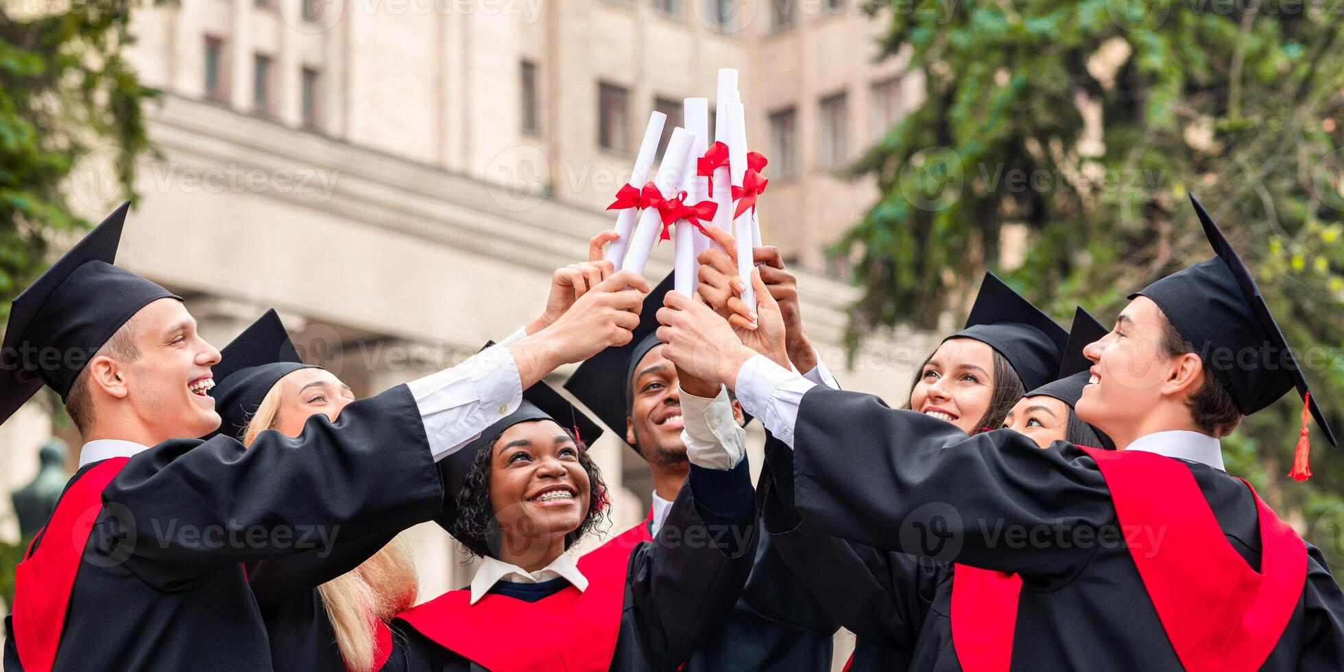 Diverse International Students Raising Diplomas Up, Celebrating Graduation, happy multiracial group of students in graduation caps and robes cheerfully posing at university campus, closeup, panorama photo