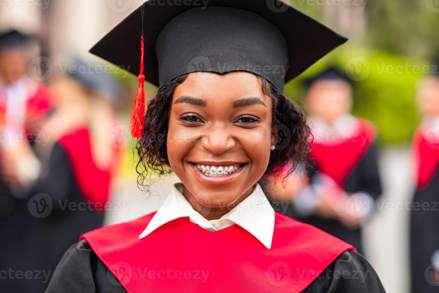 Closeup portrait of happy young black lady student wearing graduating costume. Happy african american female student celebrating graduation with her friends at university campus, blurred background photo