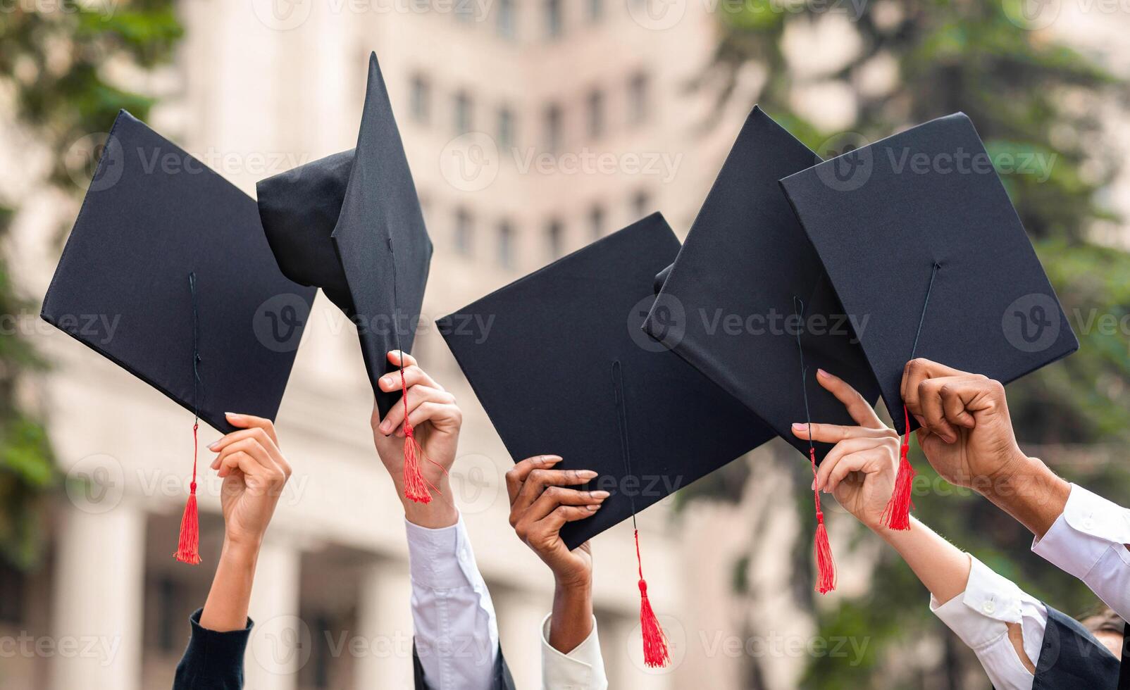Graduation concept. Cropped of multiracial group of students raising up hands with caps. Graduation hats and diplomas raised up in students hands over university or college building, closeup photo