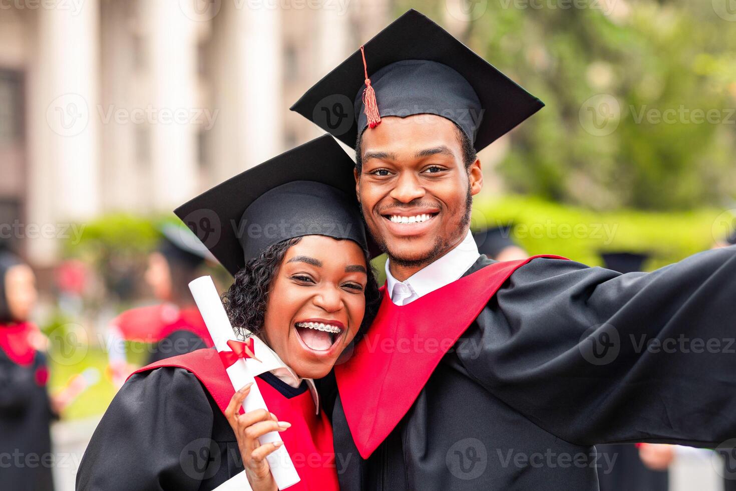Happy african american couple students in graduation dresses and hats taking selfie together, posing at university campus, enjoying and celebrating graduation, closeup portrait photo