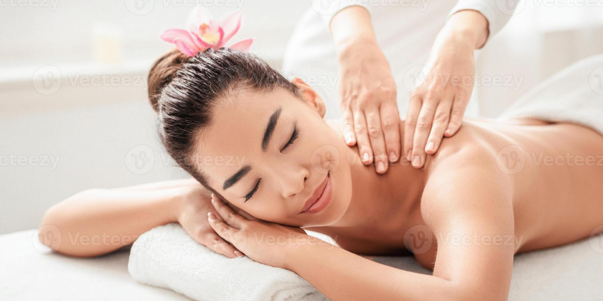 Wellness Concept. Attractive Asian Woman Relaxing During Thai Massage Session At Salon, Young Lady Lying On Spa Table With Closed Eyes, Enjoying Body Treatment From Professional Masseur, Closeup photo