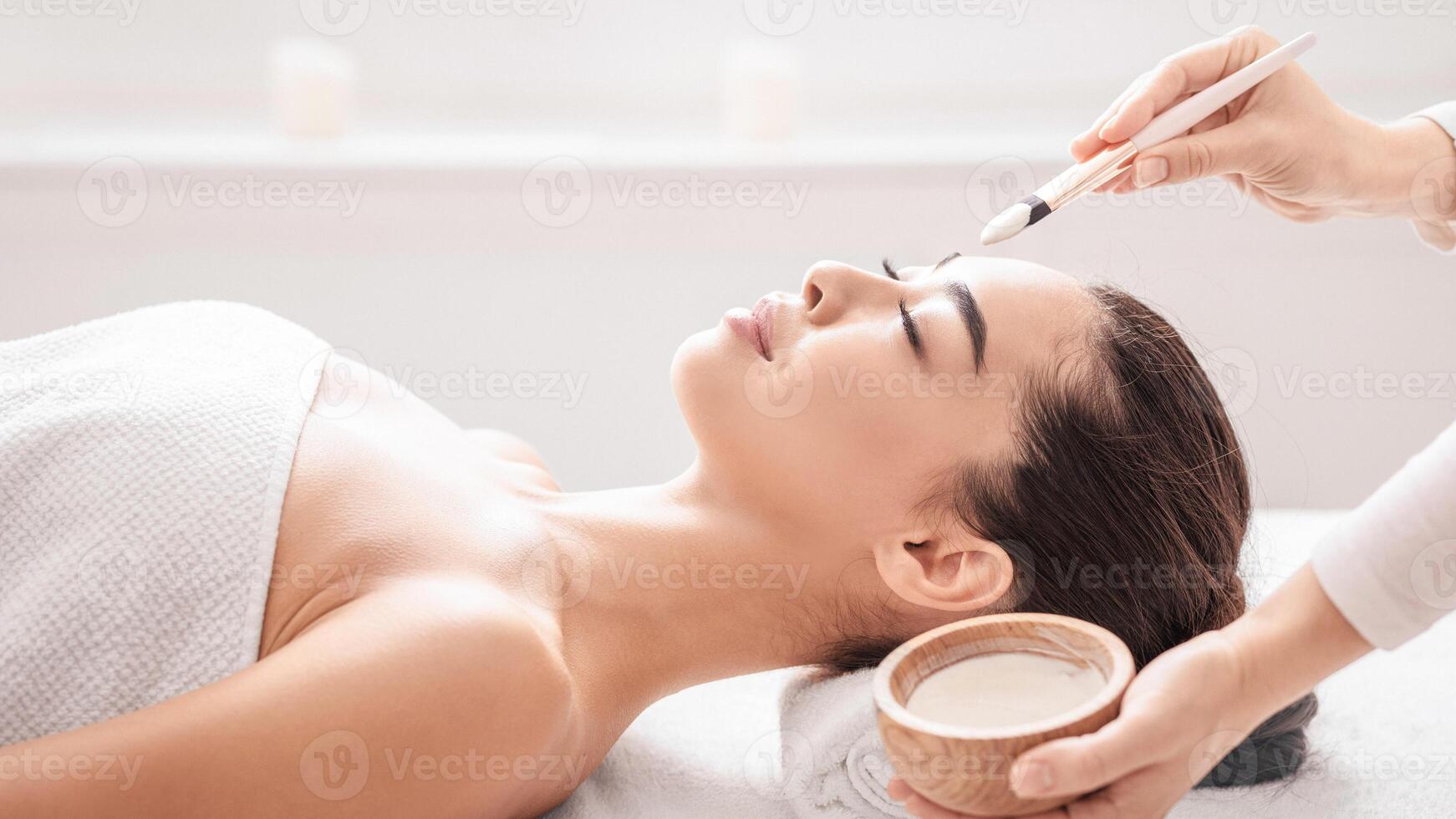 Professional Cosmetology. Beautician At Spa Salon Applying Clay Face Mask To Young Asian Woman, Relaxed Korean Female Enjoying Wellness And Skin Care Treatments, Side View With Free Space photo