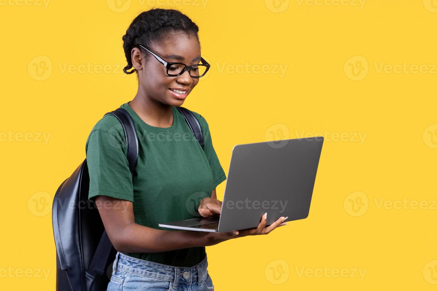 Cheerful Black Student Woman Using Laptop Standing Over Yellow Studio Background, Side View. Remote Education, E-Learning And Online Study Concept. Panorama With Copy Space photo