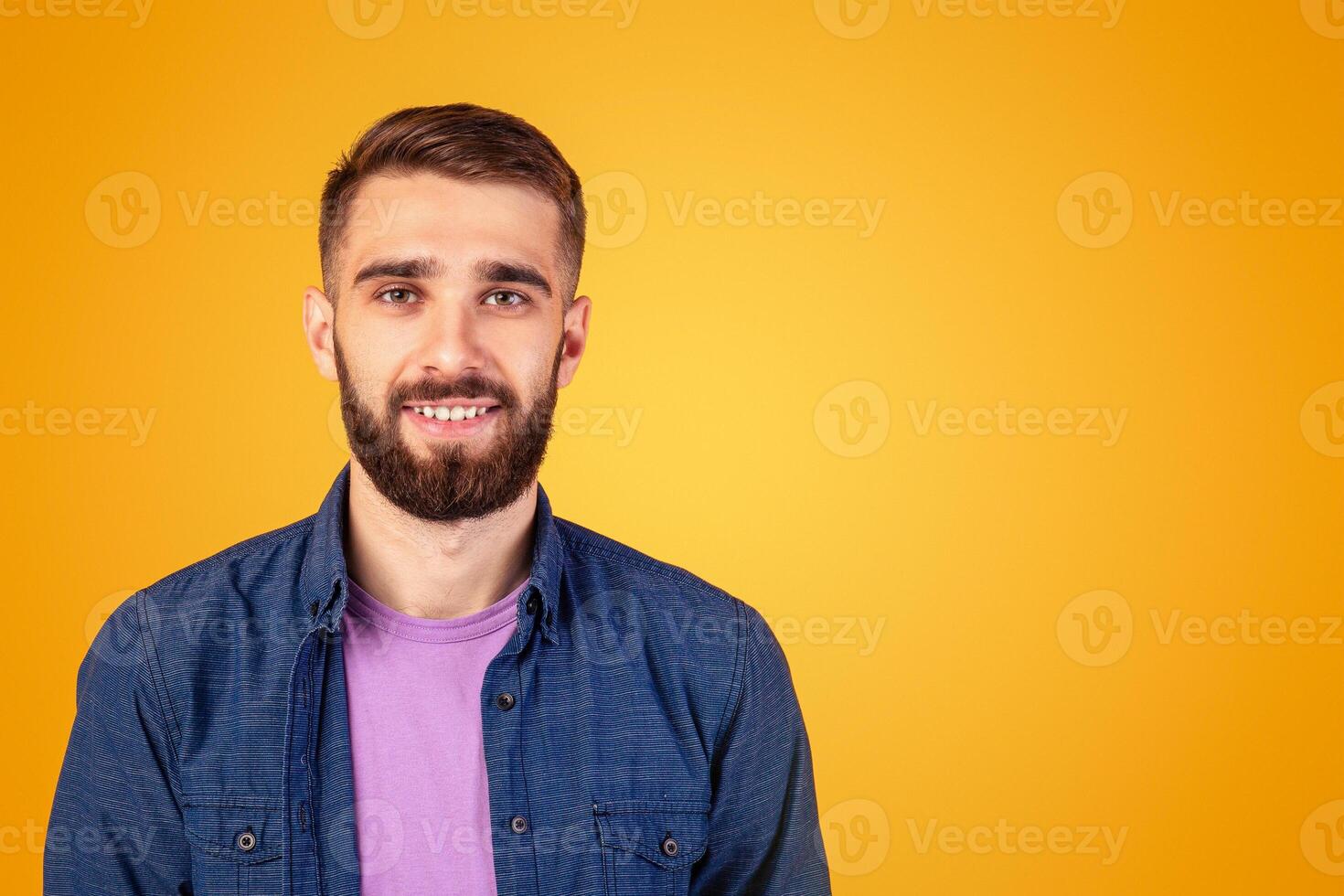 Carefree young guy looking at camera and smiling over orange studio background, panorama. Portrait of joyful bearded hipster man with happy face expression posing in casual outfit photo