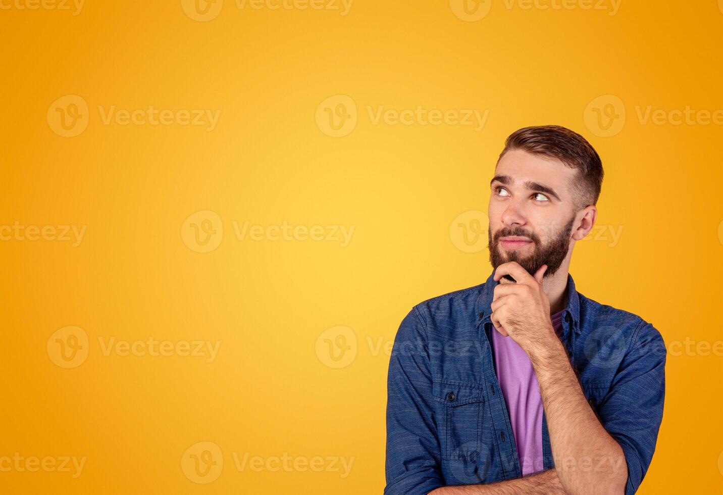 Dreamy hipster guy thinking over something, looking at empty space on orange studio background. Pensive young man making choice or decision, being thoughtful, having doubts photo