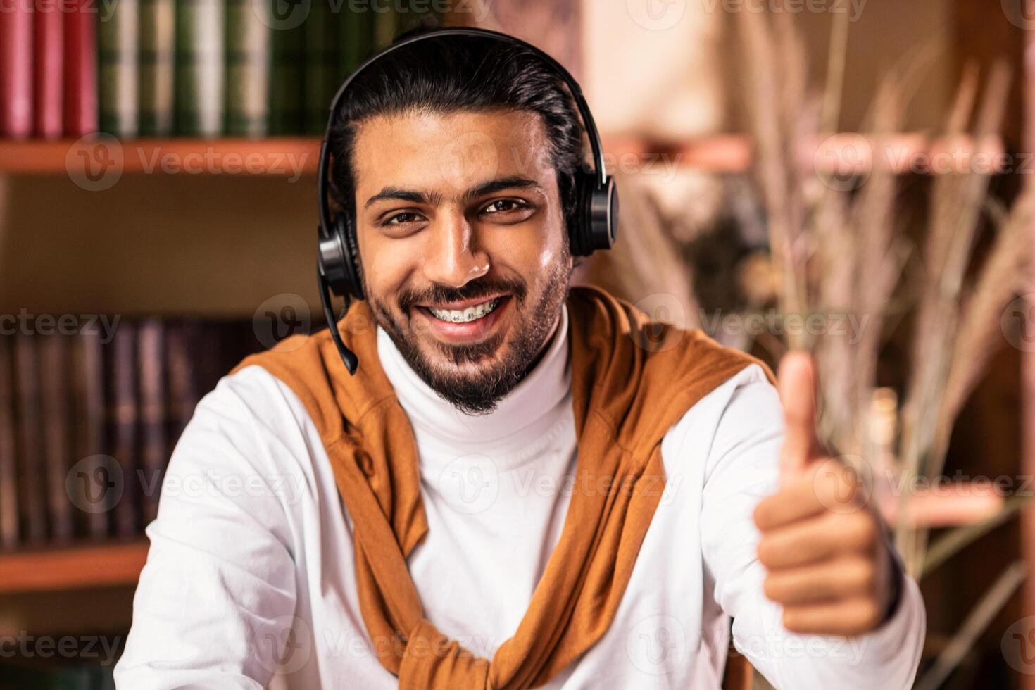 I Like Distance Learning. Cheerful Indian Student Guy Gesturing Thumbs Up Smiling To Camera Sitting At Home Near Book Shelves. Remote Online Education, Tutoring And Teaching Concept photo