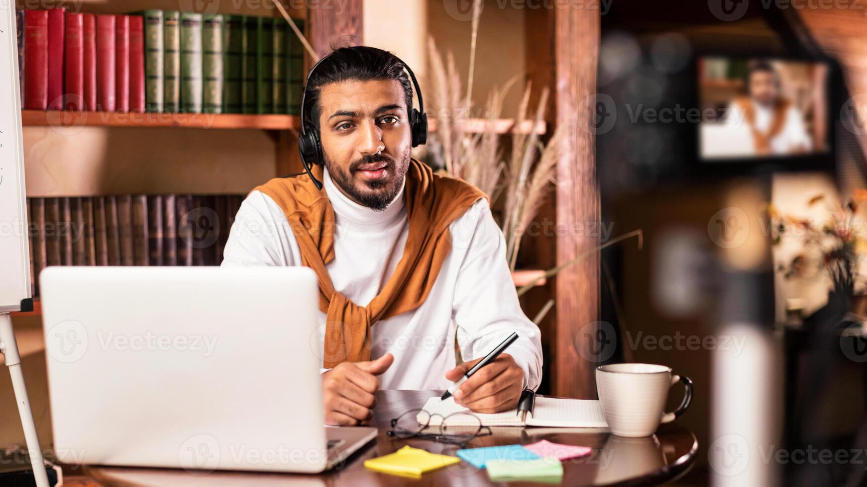 Modern Teacher. Arab Man Recording Virtual Lecture For Educational Blog Sitting In Front Of Laptop And Camera Indoors. Remote Tutoring And E-Teaching Concept. Selective Focus photo