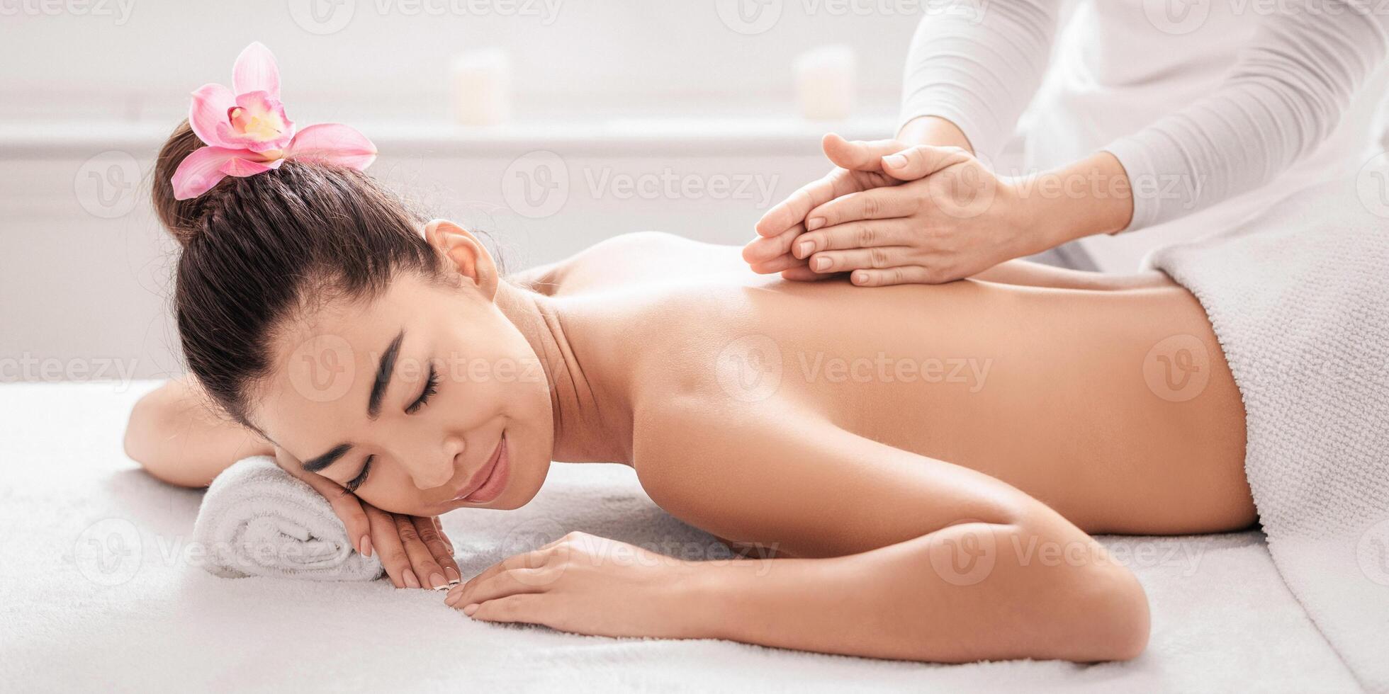 Beautiful Asian Woman Lying On Spa Bed, Getting Back Massage Treatment From Professional Masseur In Beauty Salon, Relaxed Korean Lady Enjoying Body Care And Self-Pampering, Side View With Free Space photo