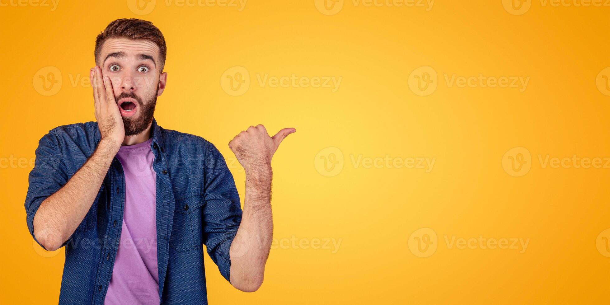 Promotion concept. Shocked hipster guy in casual outfit pointing aside at free space, recommending something, offering huge sale on orange studio background, banner design photo
