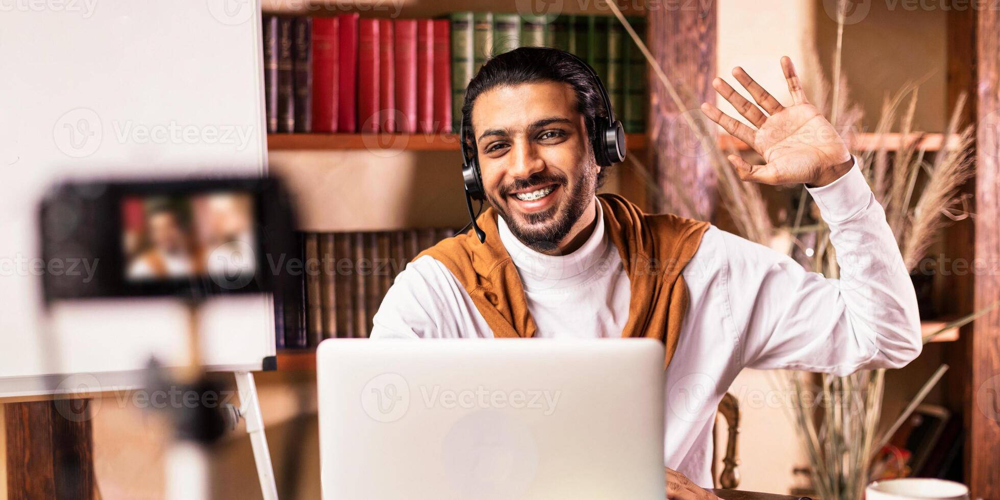 Indian Teacher Man At Laptop Teaching English Online Making Lesson For His Educational Blog Sitting At Desk At Home. Modern Education E-Teaching And Tutoring Concept. Selective Focus photo