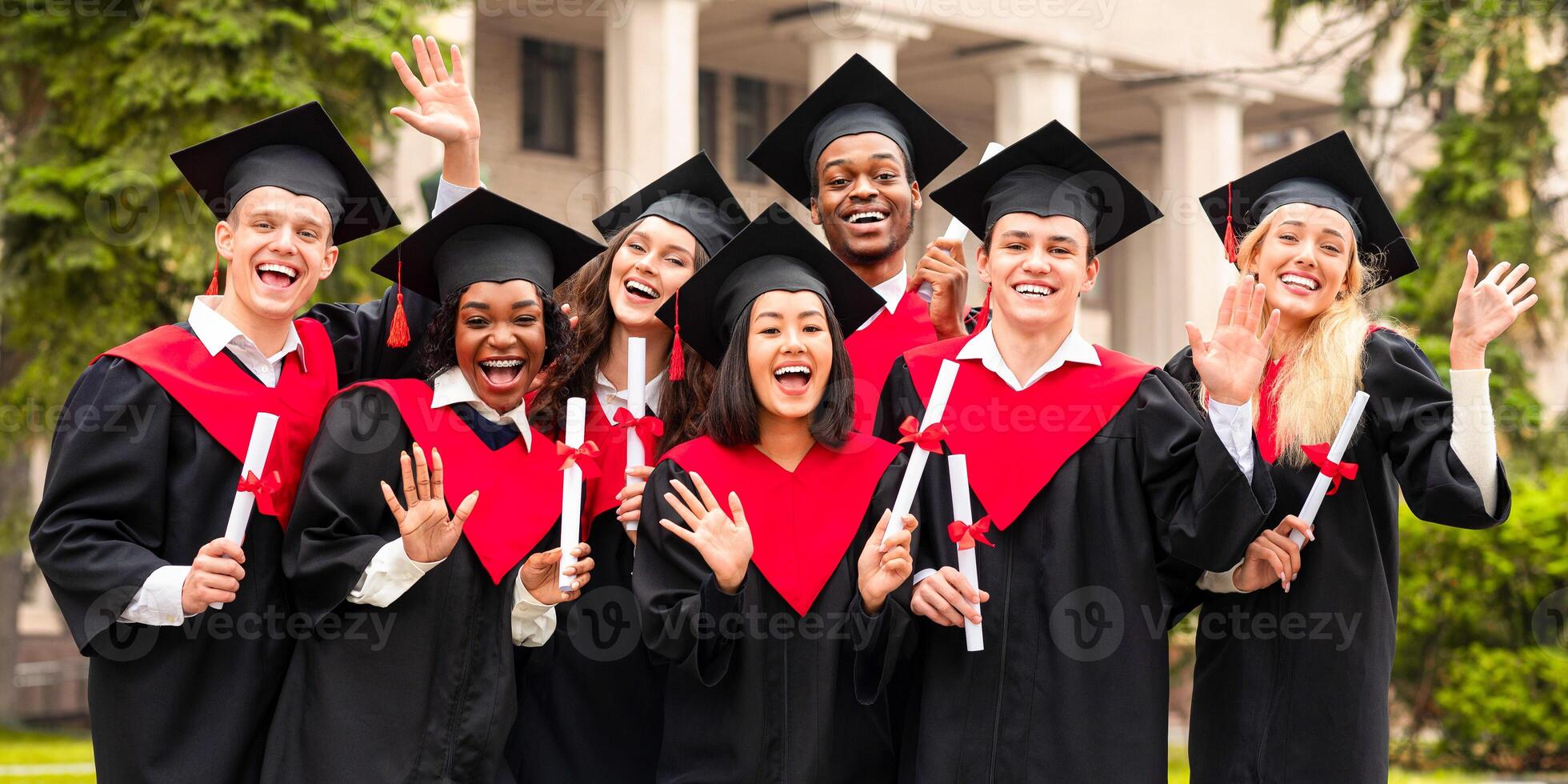Diverse International Students With Diplomas Celebrating Graduation, happy multiracial group of students in graduation caps and robes cheerfully posing at university campus, waving at camera photo