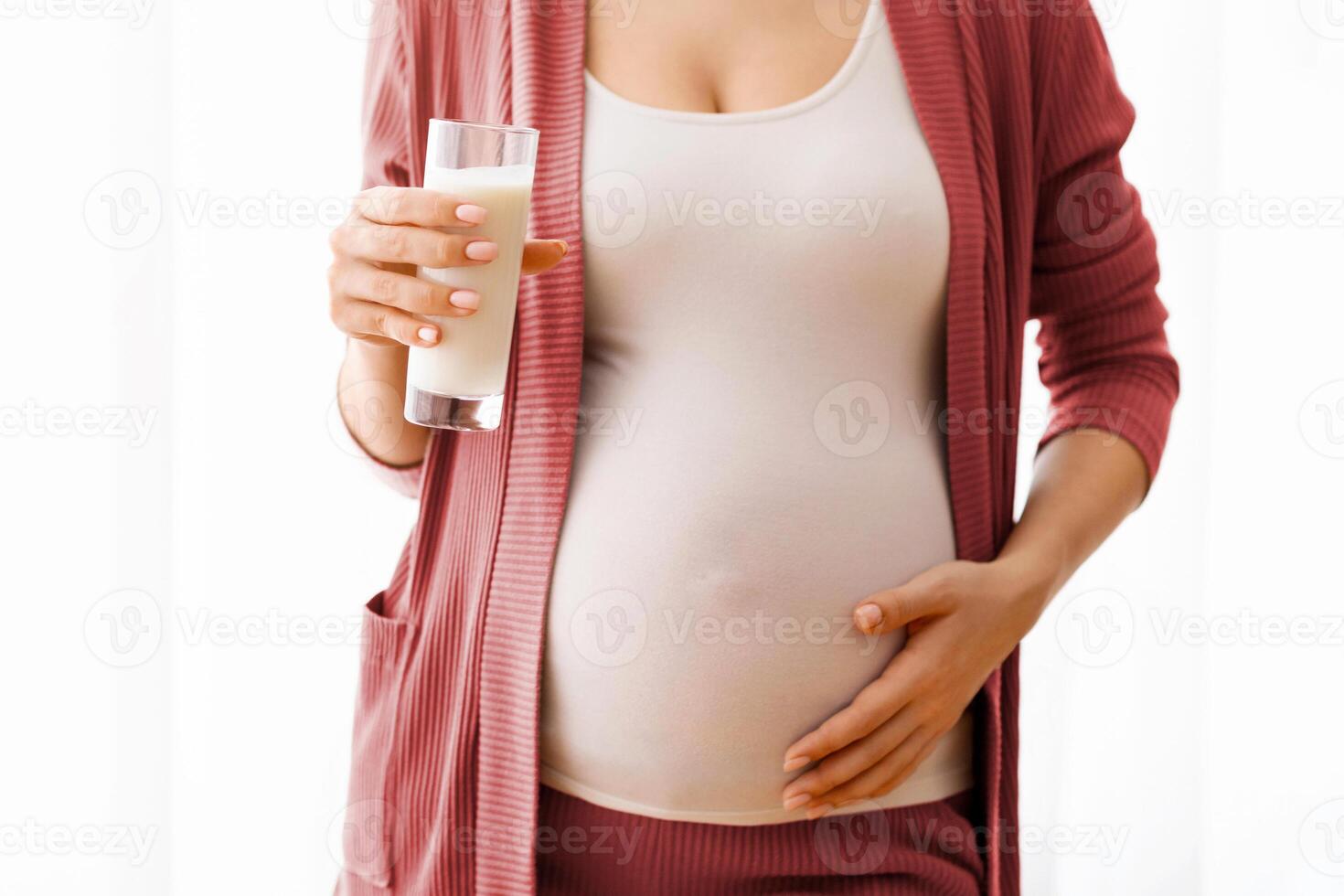 Dairy Products During Pregnancy. Closeup Shot Of Pregnant Lady Holding Glass Of Milk, Unrecognizable Expectant Mother Standing Near Window At Home And Embracing Her Belly, Cropped Image, Free Space photo