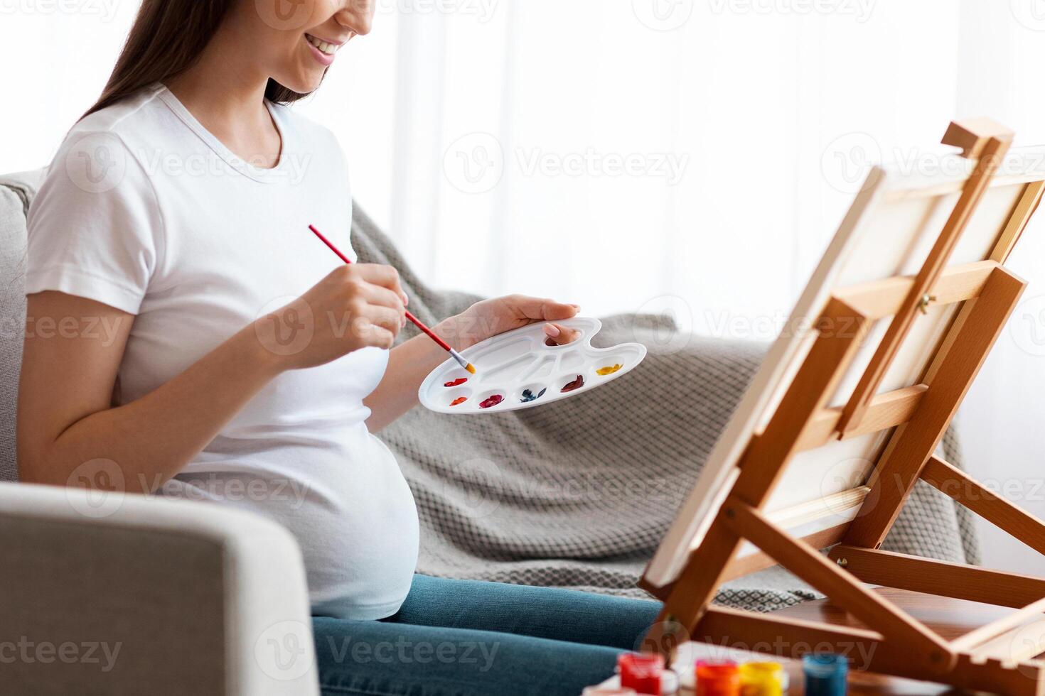 Positive Pregnant Woman Painting On Easel, Having Art Therapy Session At Home, Happy Expectant Lady Drawing Picture While Relaxing On Couch In Living Room, Enjoying Free Time During Pregnancy photo