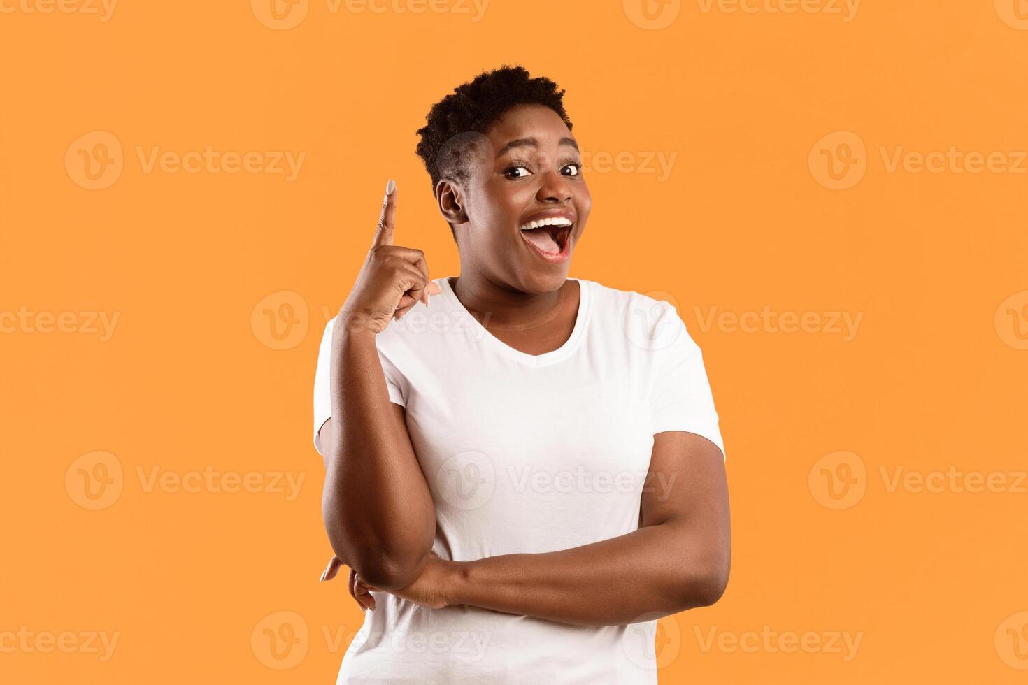 Cheerful Overweight Black Woman Pointing Finger Up Having Great Idea Posing Smiling To Camera Standing On Yellow Studio Background. Inspiration, Eureka Moment Concept photo