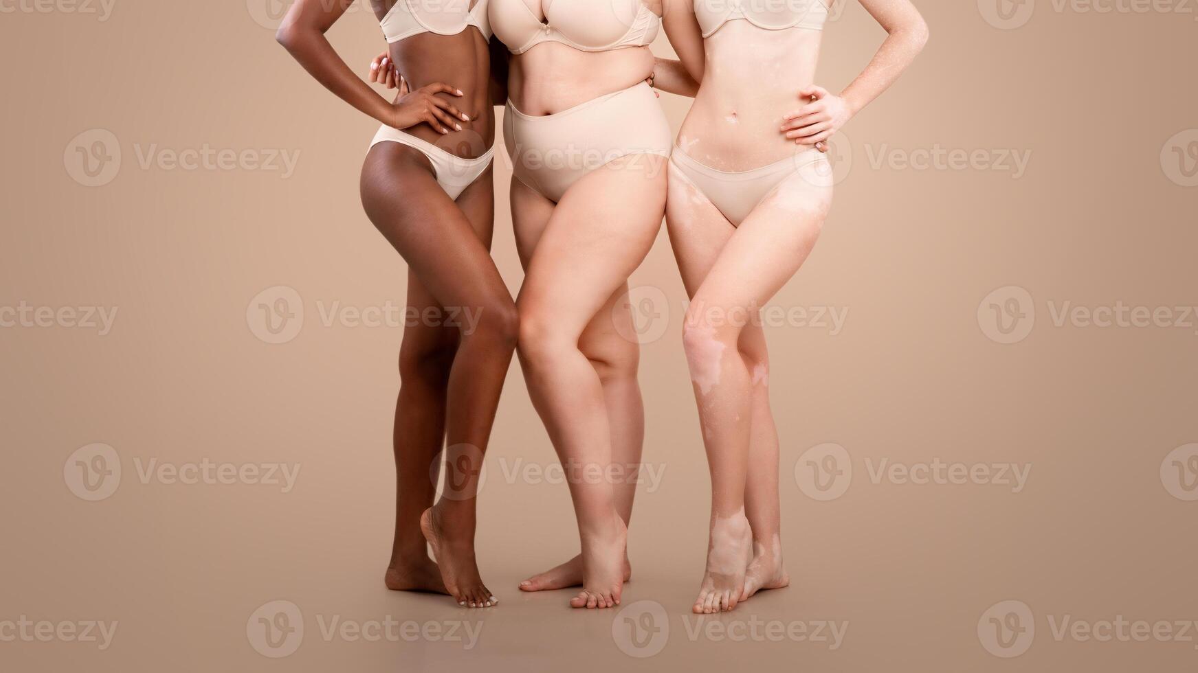 Group Of Diverse Woman In Underwear Standing Together On Beige Background In Studio, Cropped Image For Body Positive Concept. Bottom Part Of Multi-Ethnic Ladies Posing In Lingerie, Copy Space photo
