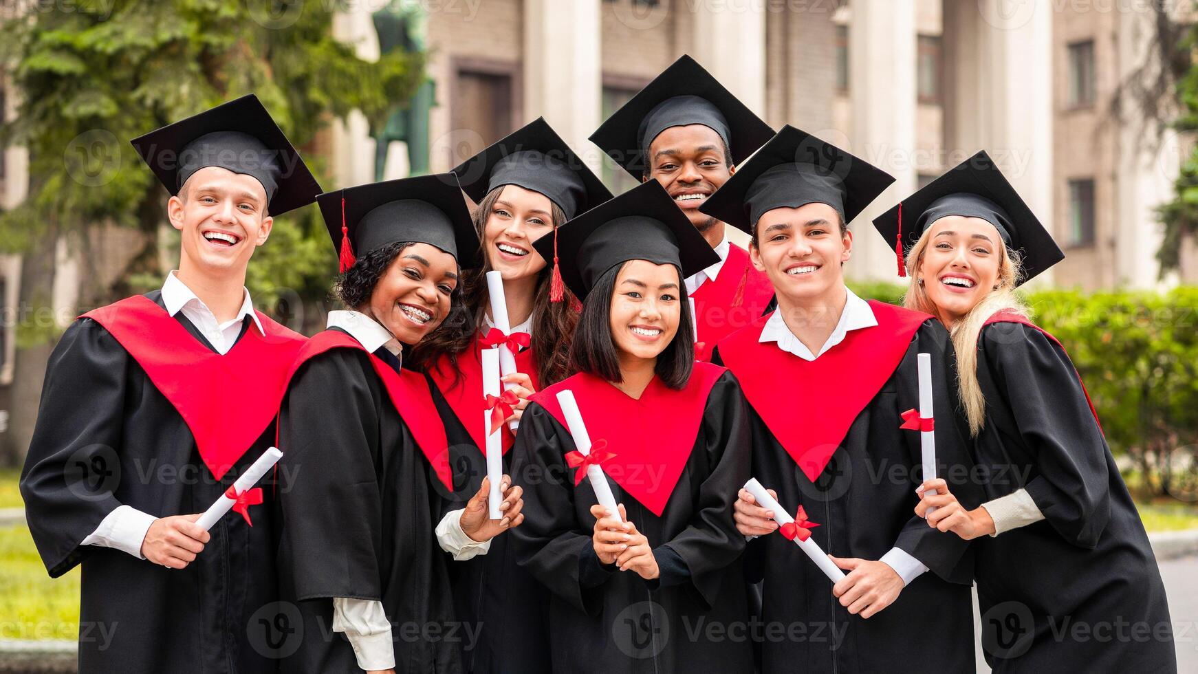 Cheerful multiracial students in graduation robes and hats celebrating graduation at university campus, posing together outdoors, smiling at camera, closeup group portrait photo