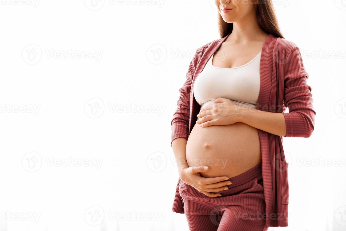 Maternity Concept. Portrait Of Young Beautiful Pregnant Lady Standing Near Window At Home, Dreamy Expectant Woman Tenderly Embracing Her Naked Belly And Smiling, Enjoying Prenatal Time, Copy Space photo
