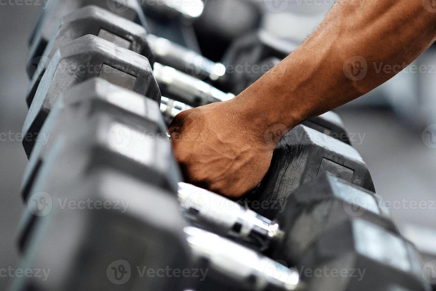 Sports equipment for gym concept. Hand of unrecognizable african american muscular bodybuilder grabbing barbell at modern gym, copy space. Cropped of black athletic man working out with dumbbells photo
