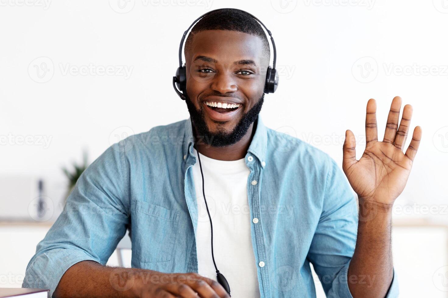 Videocall screenshot of happy young black man in headset having web conference. Positive african american guy waving hand at camera, gesturing hello, enjoying online communication, webcam view photo
