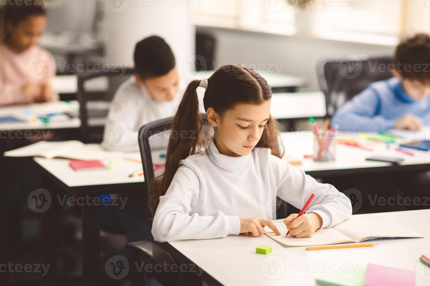 Cute female pupil sitting at desk in classroom at the elementary school. Student girl doing test in primary school. Children writing notes during the lesson or drawing picture in diary photo