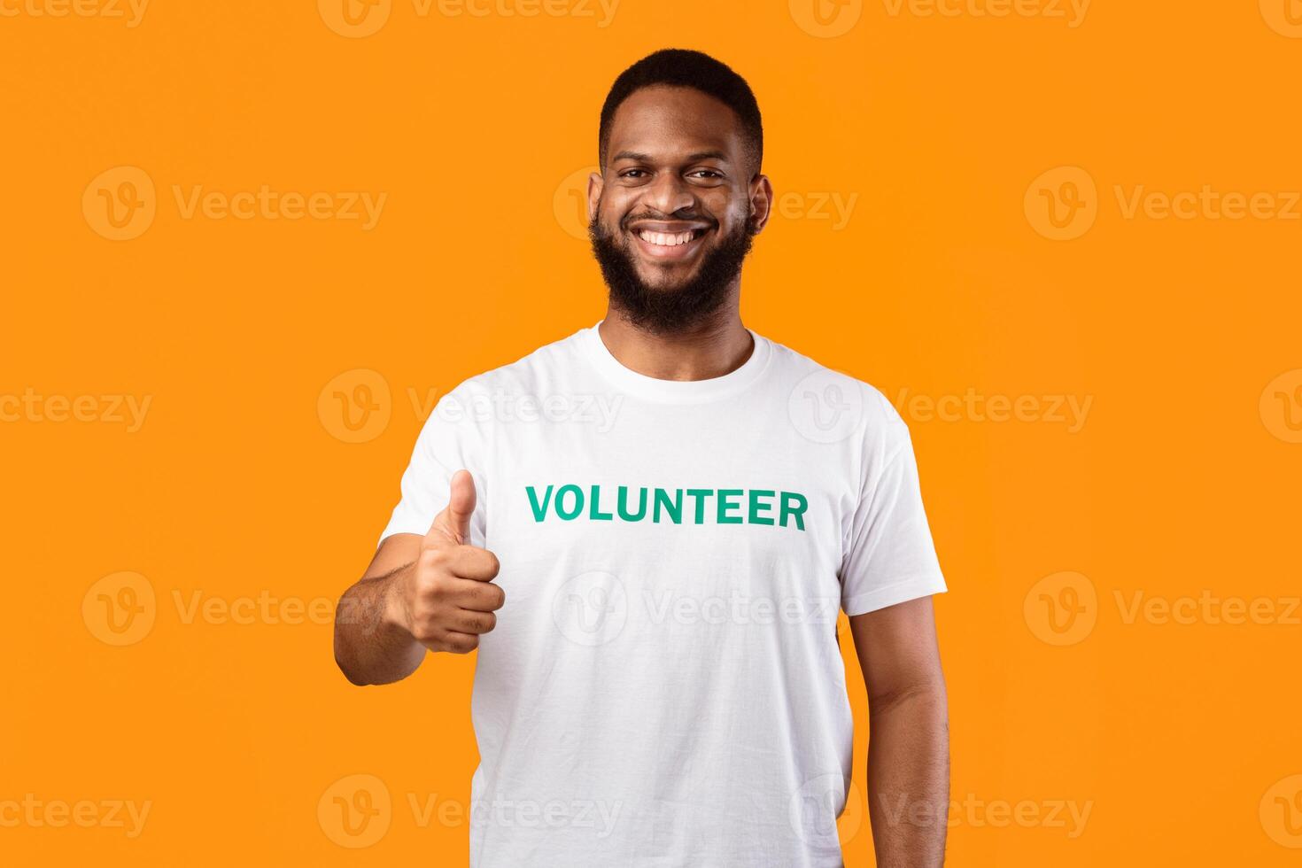 Happy African American Male Volunteer Gesturing Thumbs Up Posing Standing Over Yellow Studio Background, Smiling To Camera. Activist Guy Approving Charity Work With Like Gesture photo
