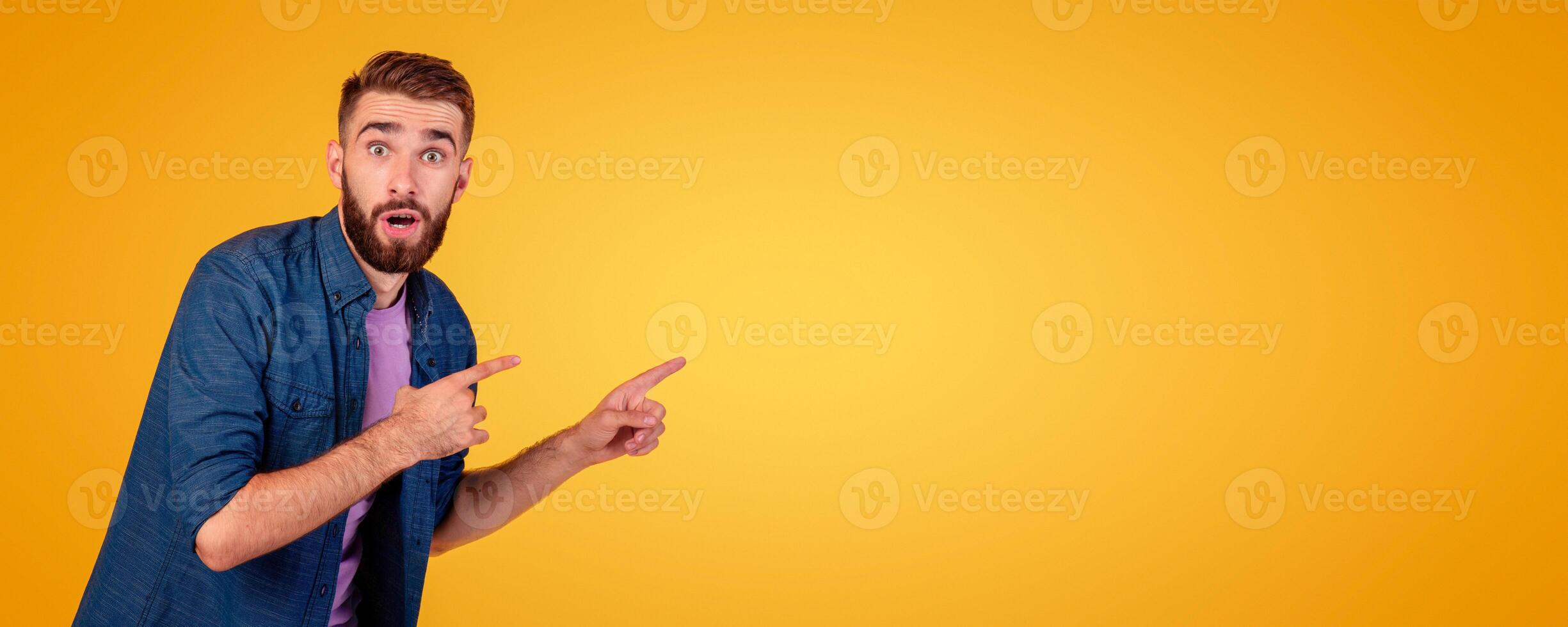 Emotional Caucasian guy pointing aside at blank space over orange studio background, banner design. Portrait of shocked young man offering product promo, sale or discount photo