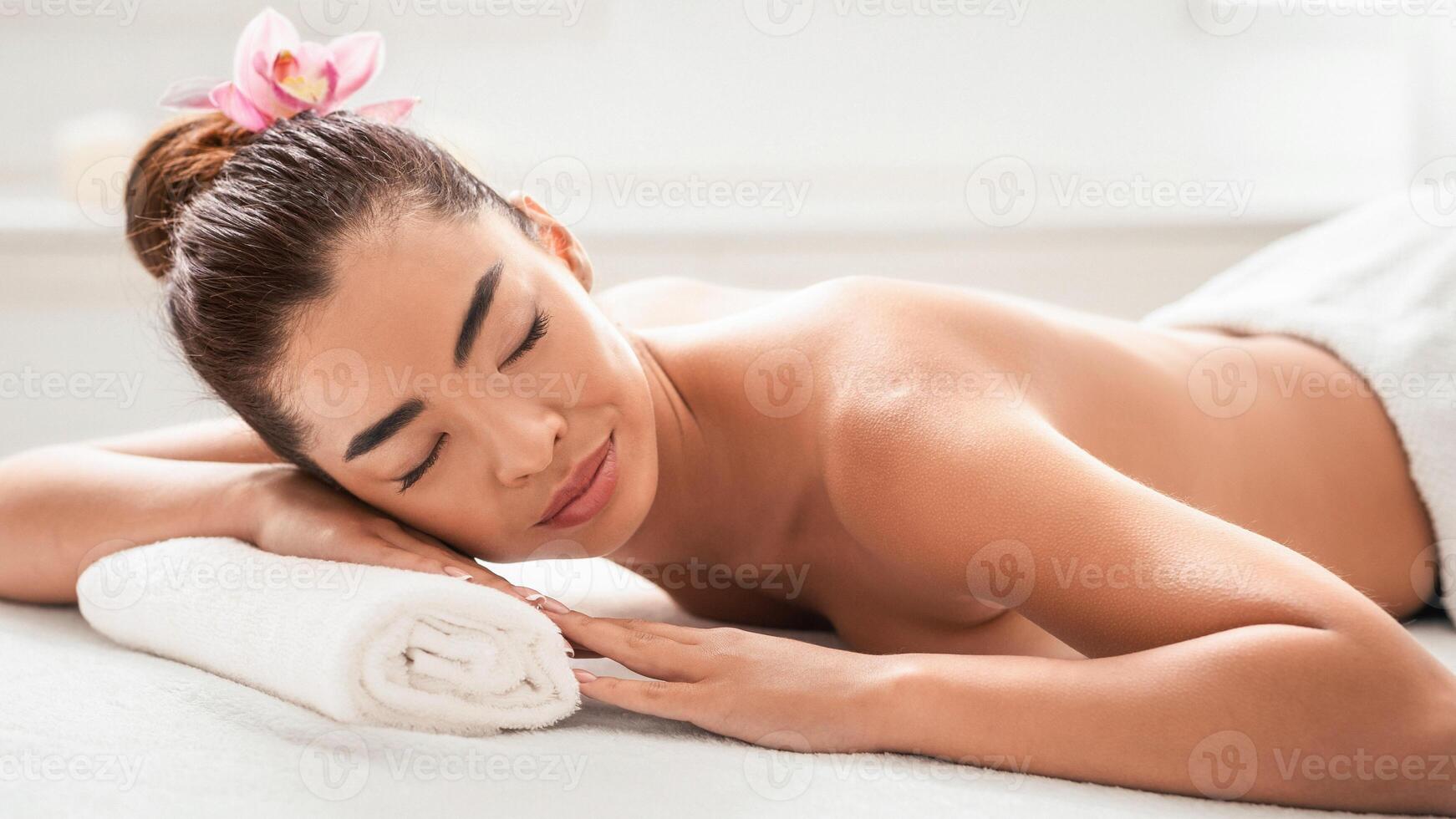 Young Beautiful Korean Woman Relaxing On Massage Table At Spa Salon, Lying With Closed Eyes, Ready For Beauty Treatments, Having Wellness Day At Beauty Parlor, Closeup Shot With Free Space photo