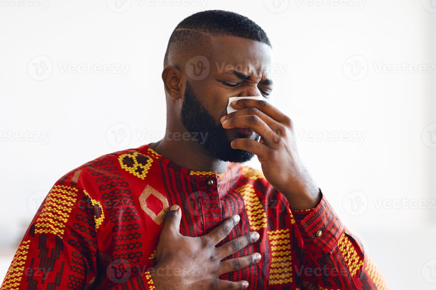 Coronavirus Symptoms. Black Freelancer Guy In Ethnic Costume Feeling Sick And Unwell At Home, Ill African American Man Suffering Runny Nose, Sitting At Desk With Laptop Computer, Copy Space photo