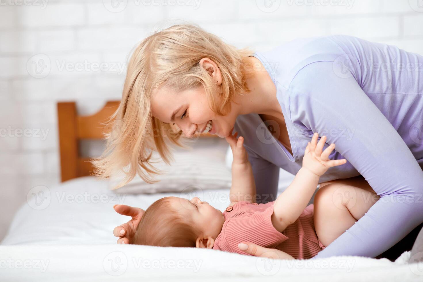 Love and tenderness, motherhood concept. Loving caucasian mother caressing her cute baby boy or girl, lying together on bed. Young woman mom bonding with little kid at home, copy space photo