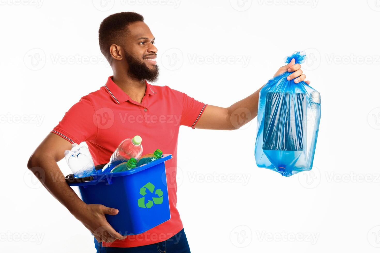 African American Guy Posing With Box Full Of Recycling Plastic And Blue Garbage Bag Standing Over White Background In Studio. Sort And Recycle Your Waste Concept, Side View photo