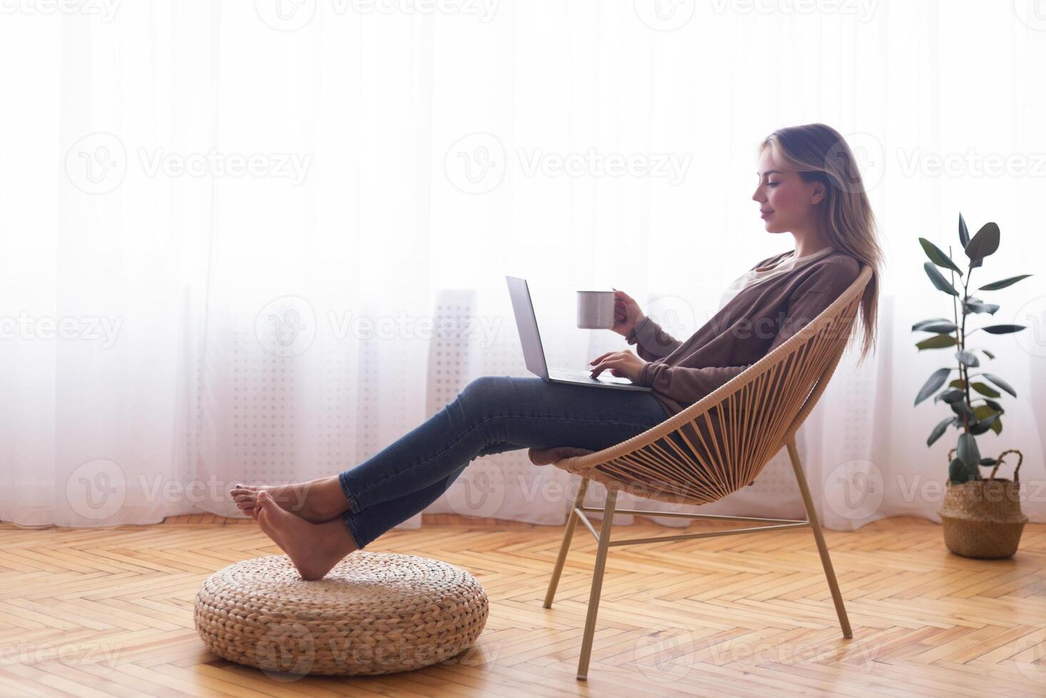 Weekend leisure. Young girl networking on laptop, relaxing with coffee near window, free space photo