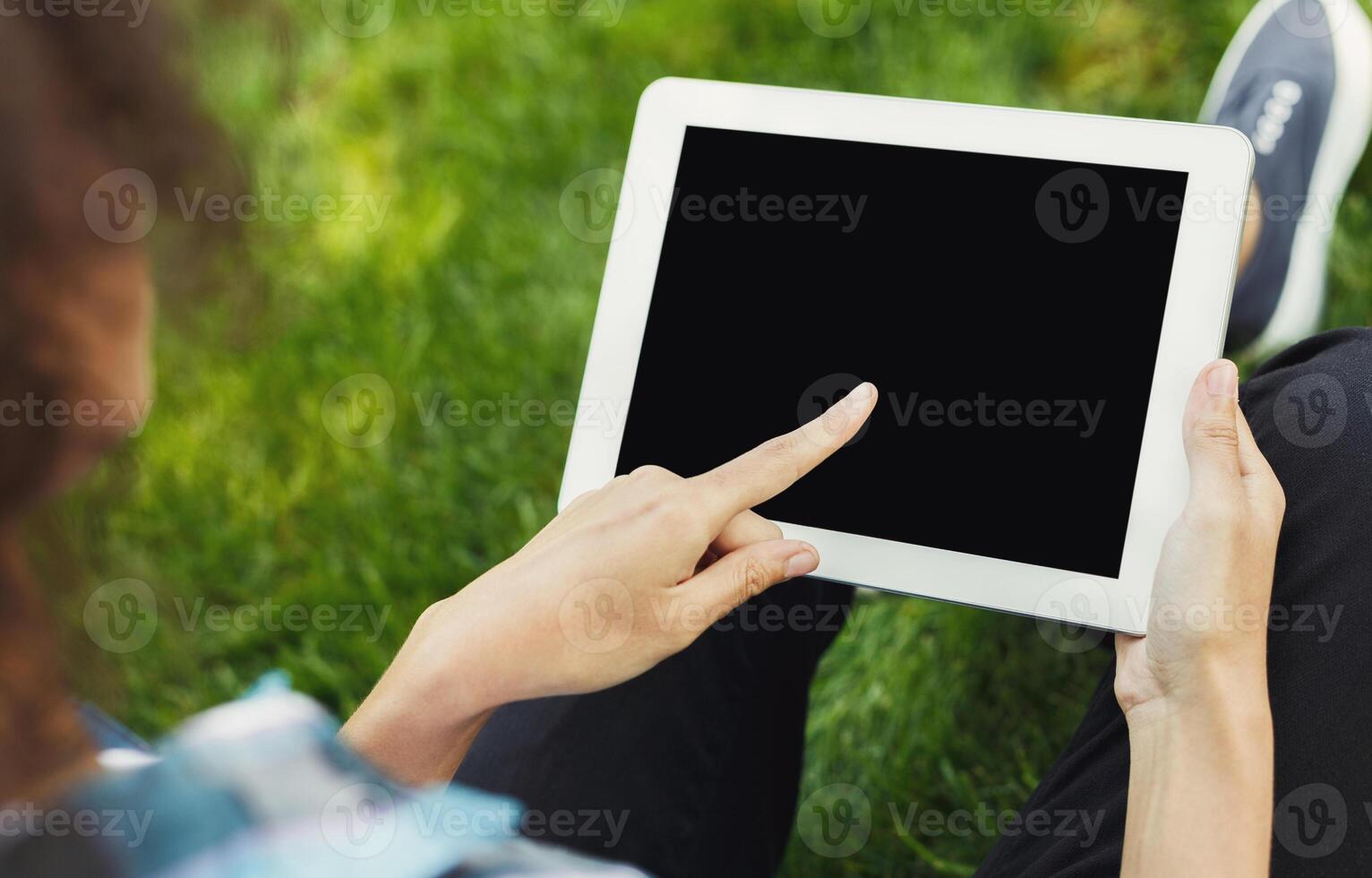 Unrecognizable woman sitting outdoors on grass with digital tablet, typing, surfing internet, preparing for exams. Technology, communication, education and remote working concept, copy space photo