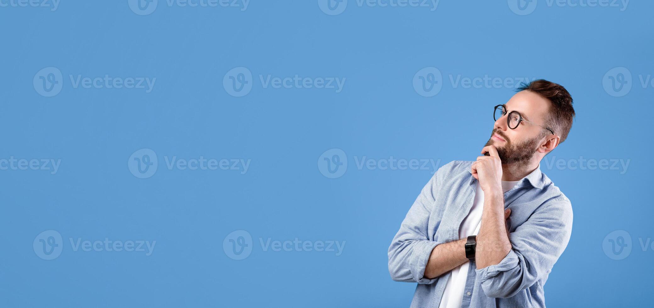Pensive Caucasian guy thinking over decision or problem, looking at empty space over blue studio background. Thoughtful bearded man hoping, imagining,making choice photo